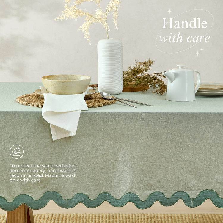 Table setting with a green tablecloth, white teapot, and decorative elements on a neutral background.