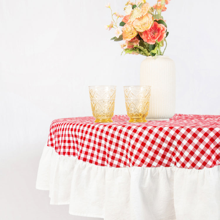 Table with red and white checkered tablecloth, two glasses, and a vase of flowers on a white background