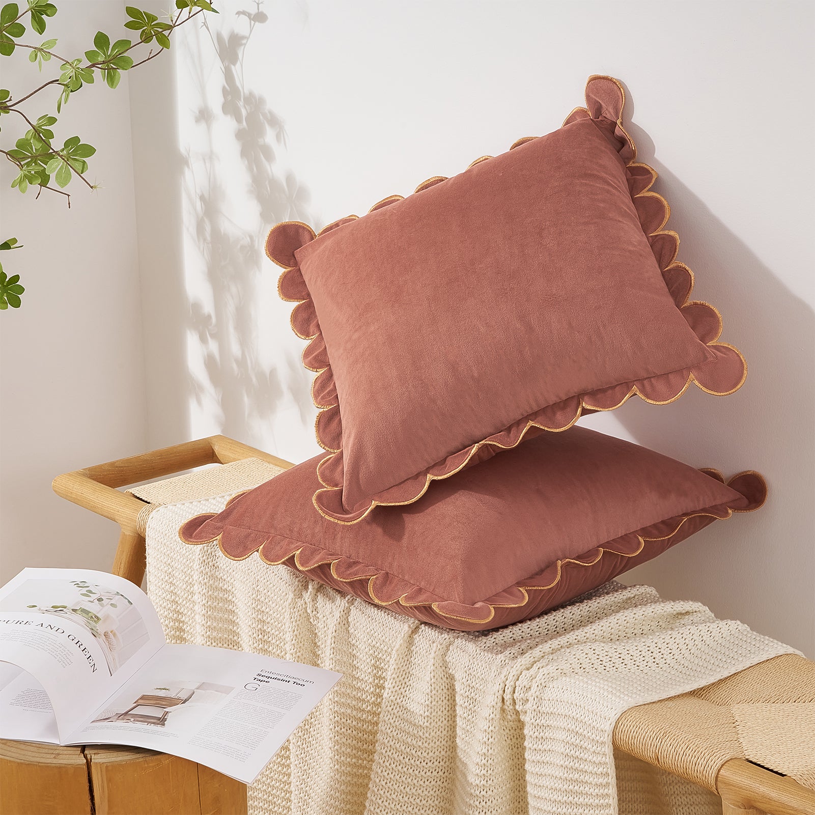 Pair of pink cushions with scalloped edges on a wooden bench with a white blanket and open book.