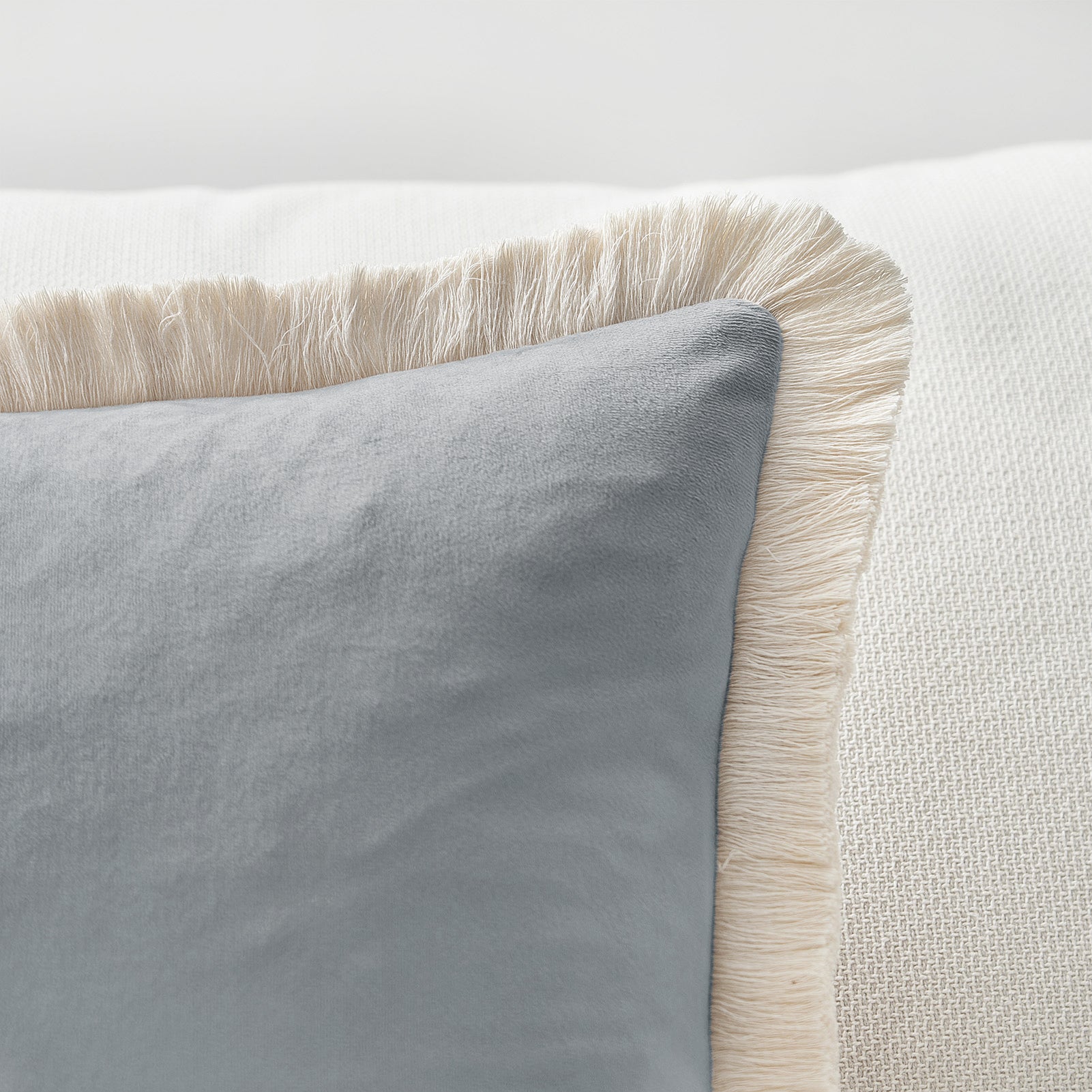 Gray pillow with beige fringes on a light gray background