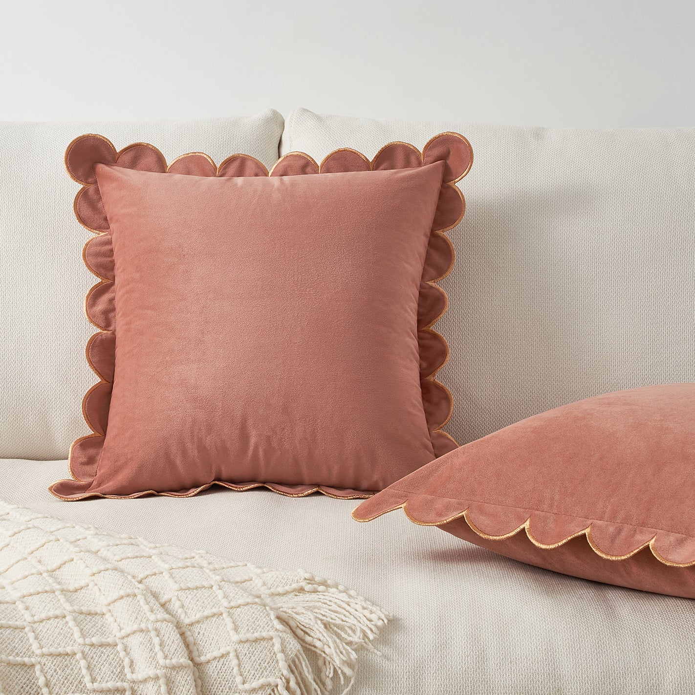 Pink scalloped-edge pillows on a light-colored sofa with a textured blanket.