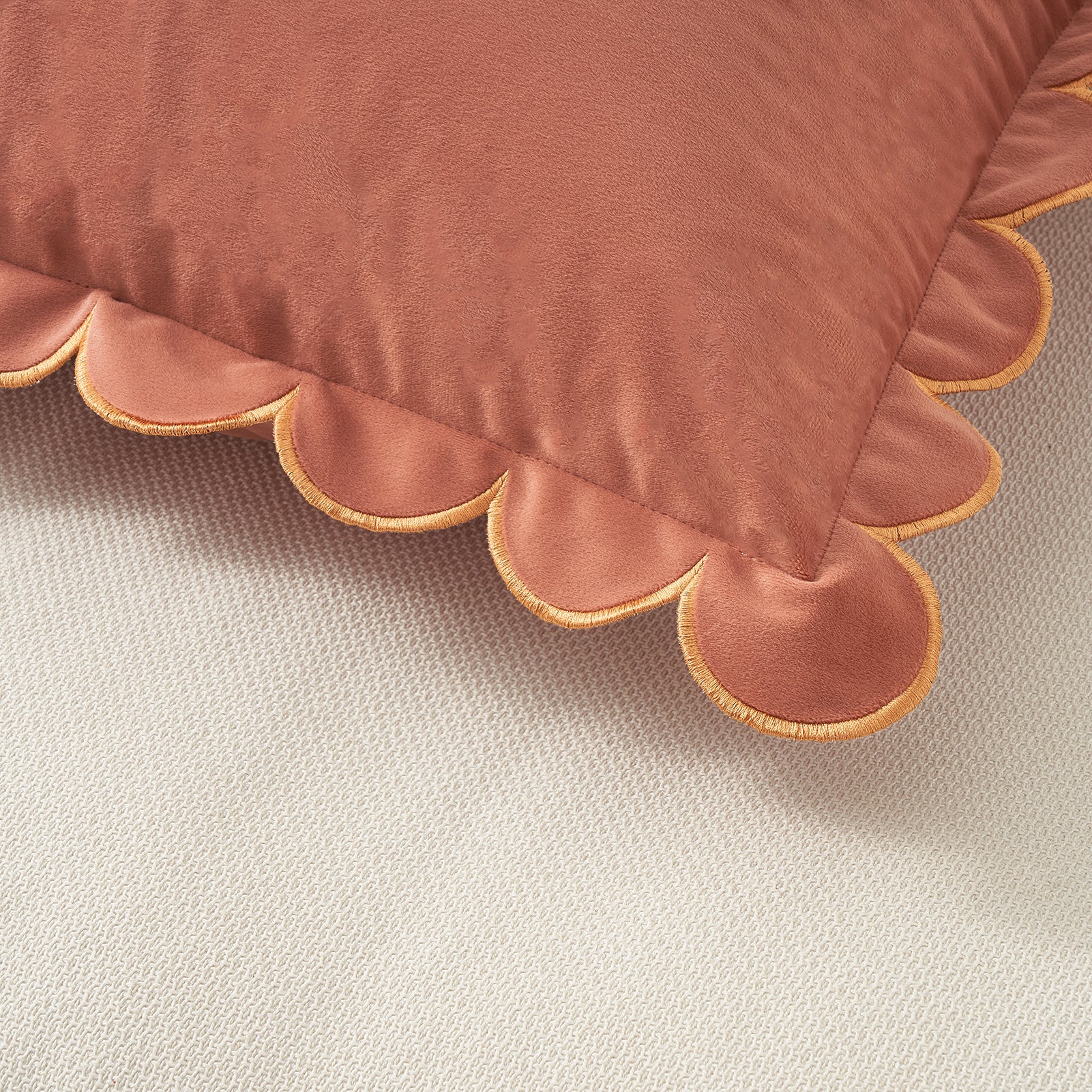 Close-up of a scalloped-edge pillow in a warm brown color on a neutral background