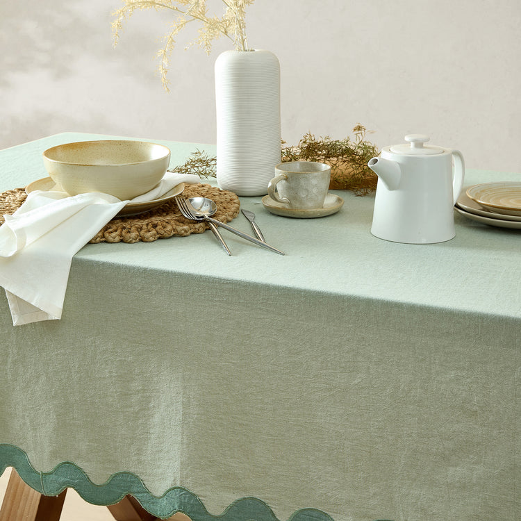 Table setting with a green tablecloth, white teapot, cup, and utensils on a light background.