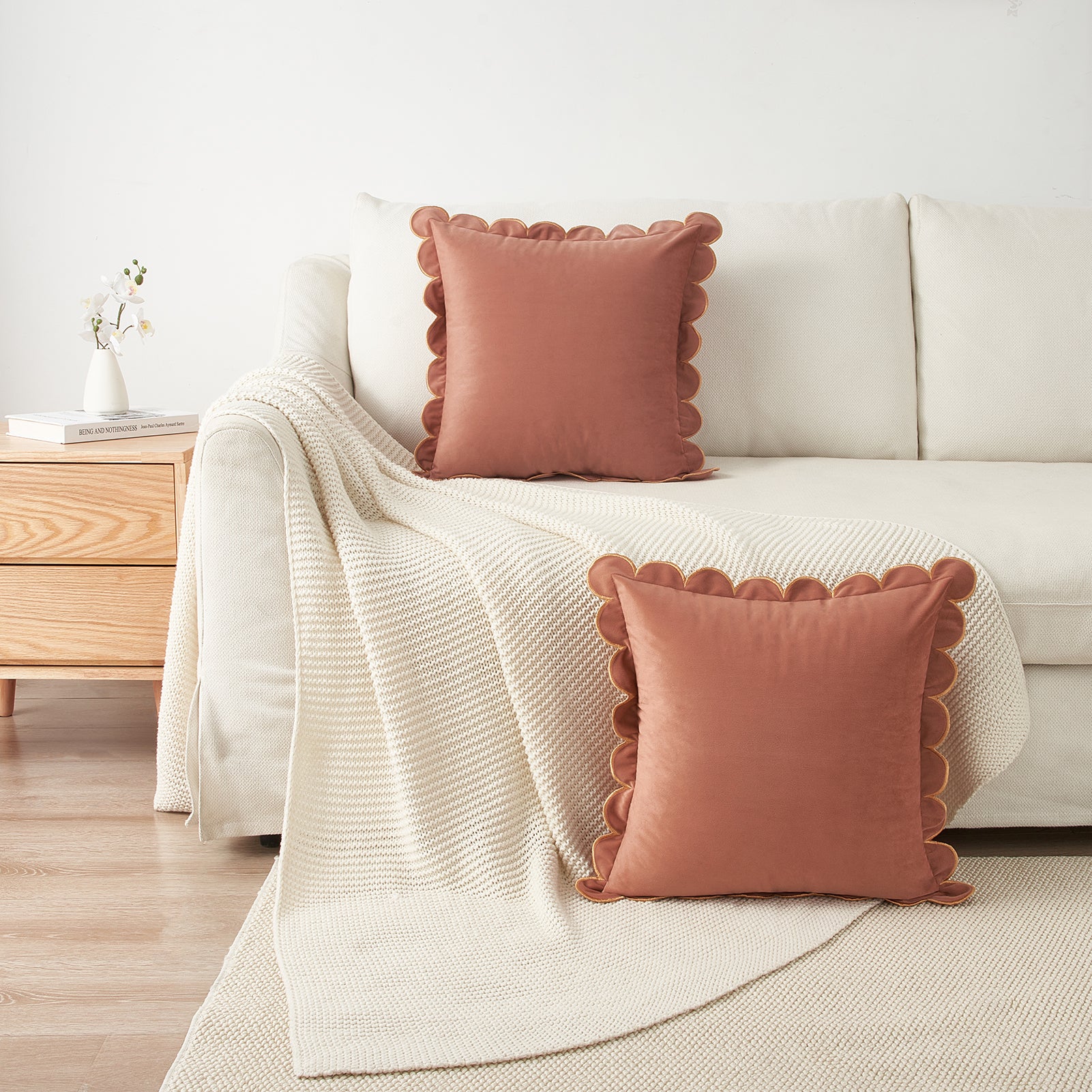 Two pink scalloped-edge pillows on a beige sofa with a white blanket, in a living room setting.