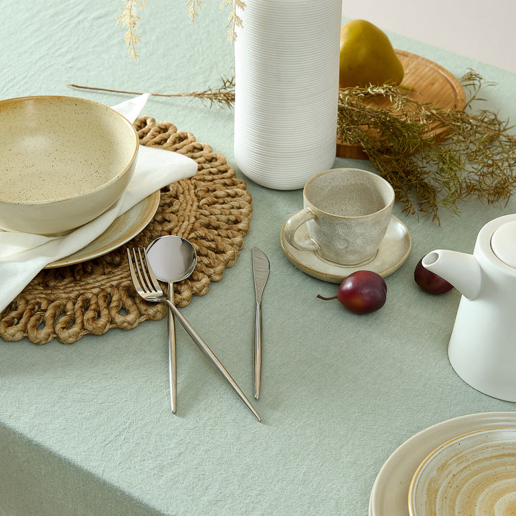 Table setting with ceramic bowls, teapot, and cutlery on a light green surface.