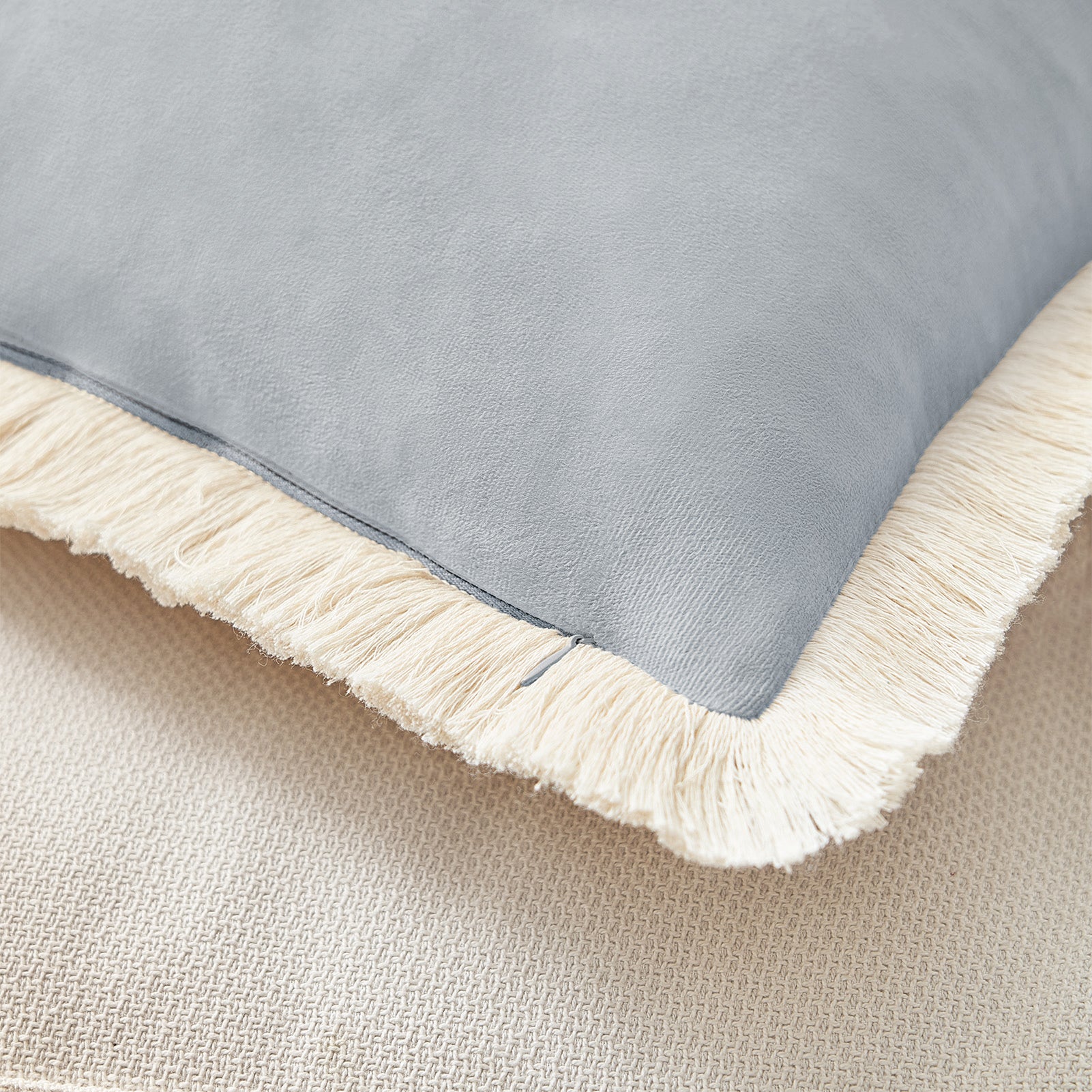 Gray blanket with white fringe on a beige surface