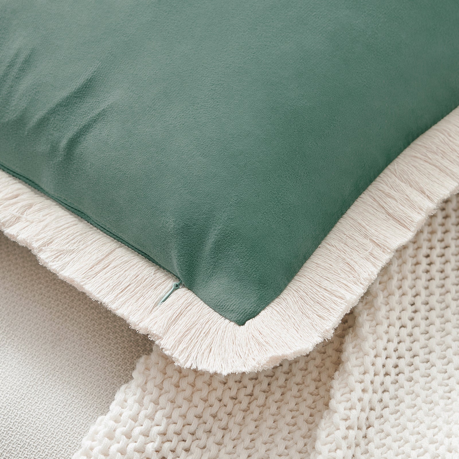 Close-up of a green pillow with white fringe on a textured beige surface