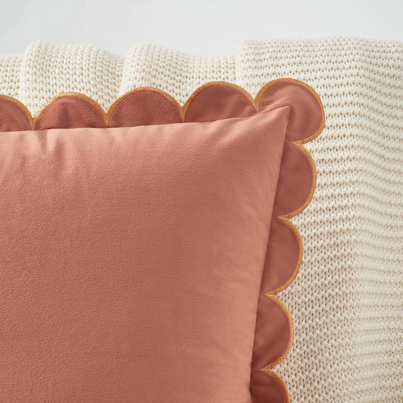 Pink pillow with scalloped edge on a textured beige surface