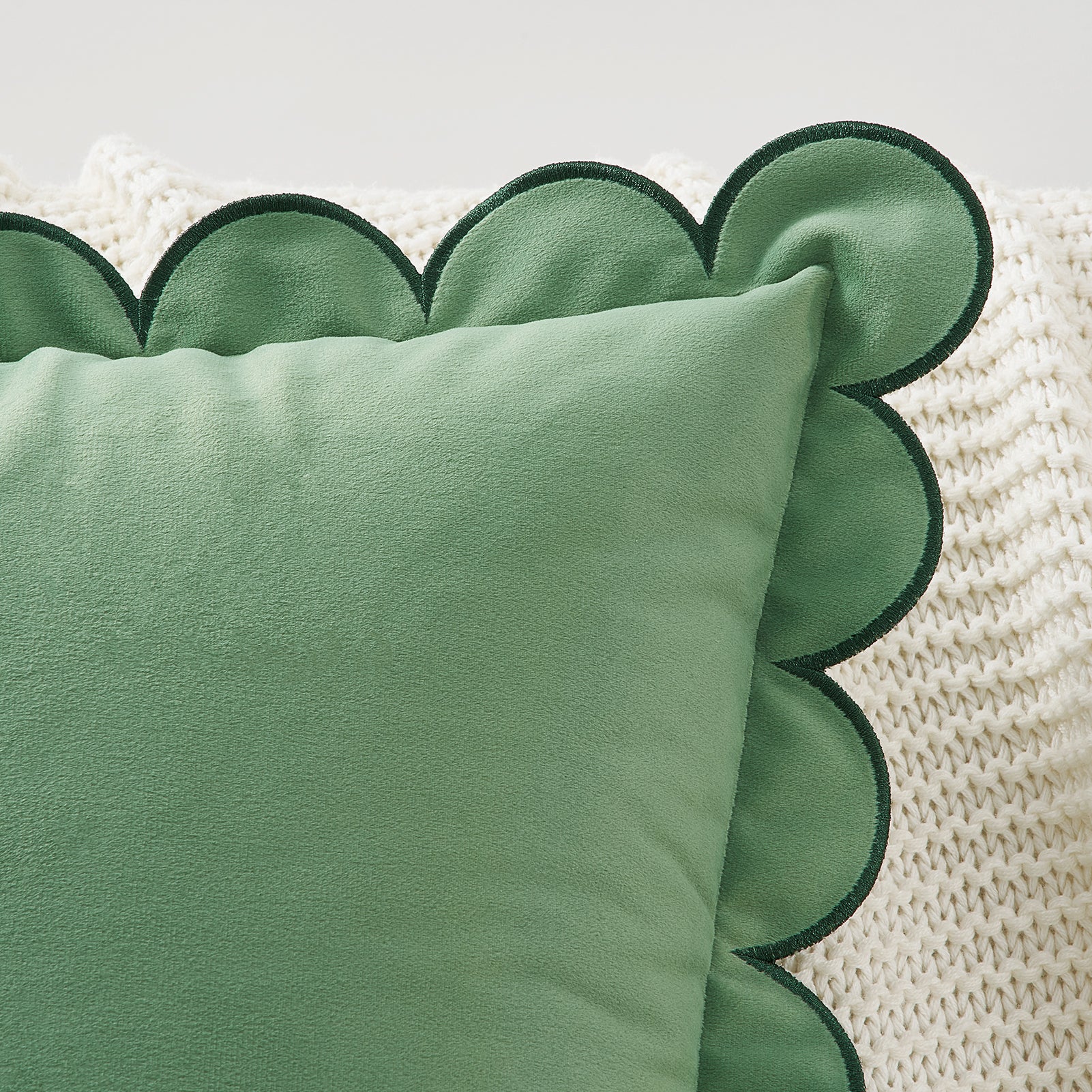 Green scalloped-edged pillow on a textured white surface