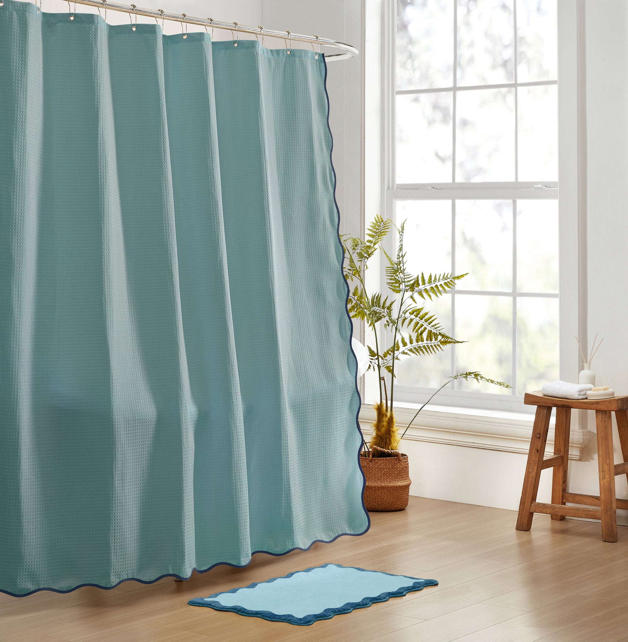 Teal shower curtain in a bathroom with a plant and stool near a window.