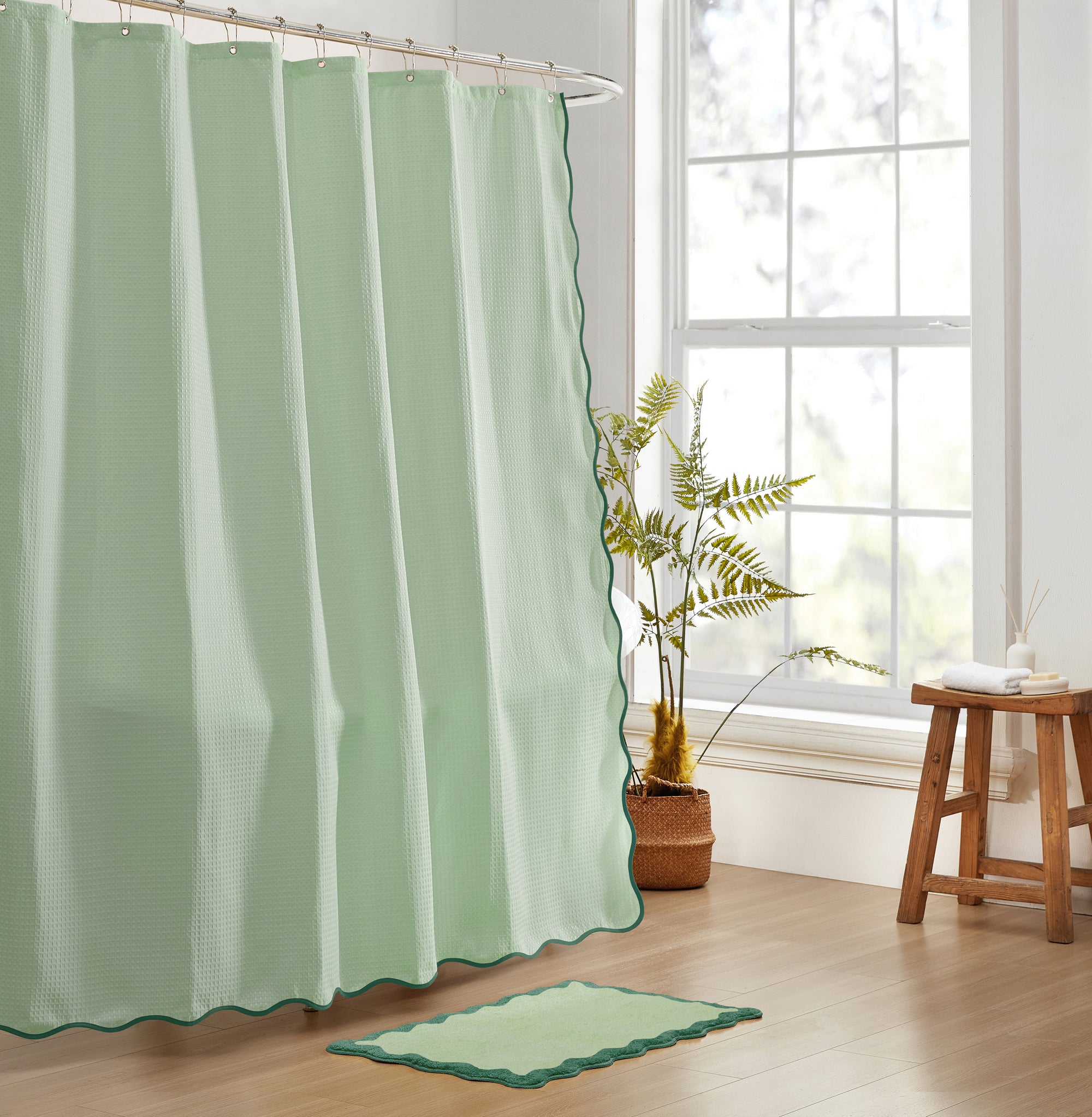 Green shower curtain and rug in a bathroom with a window and plant.