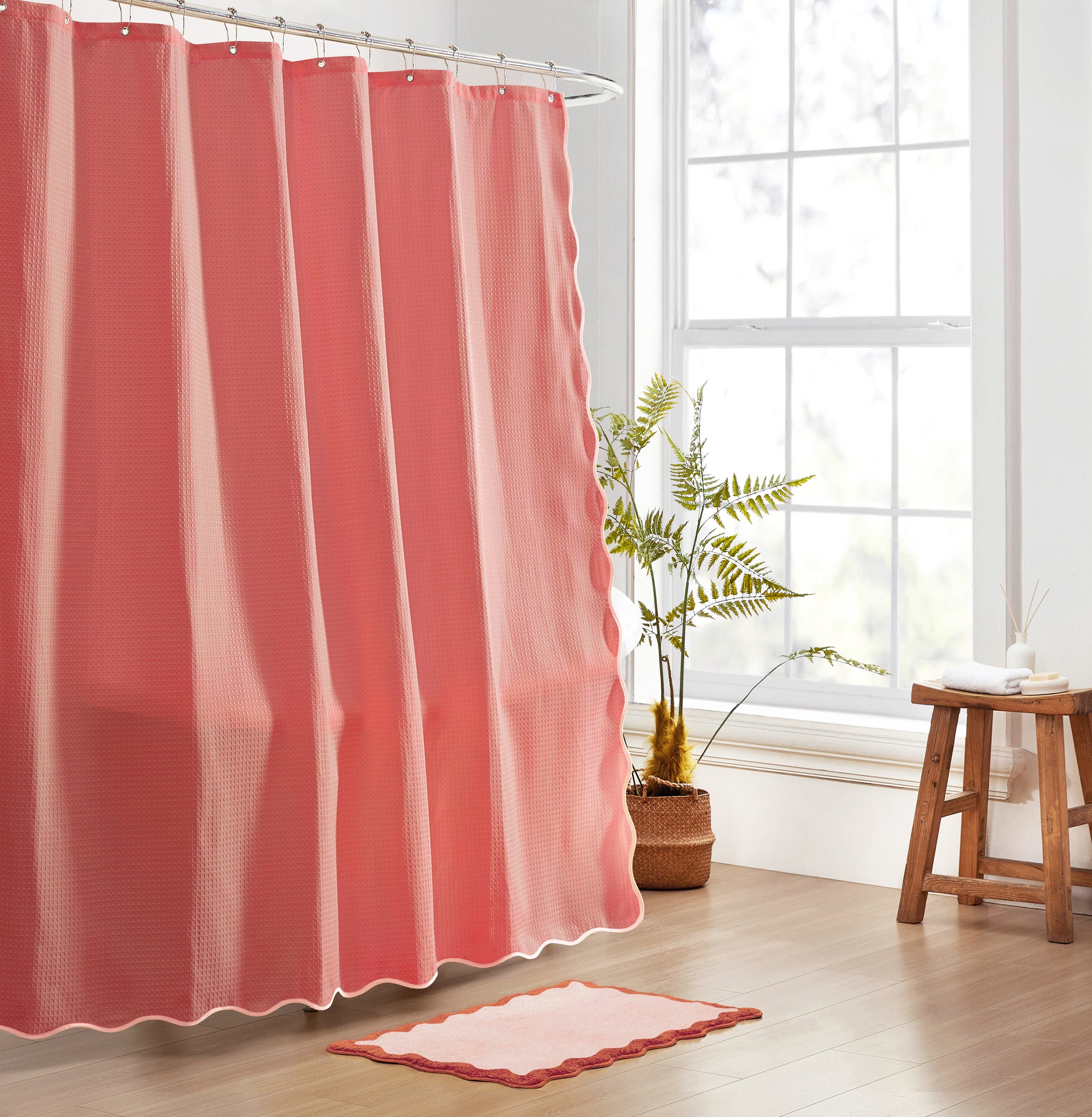 Pink shower curtain and rug in a bathroom with a plant and stool.