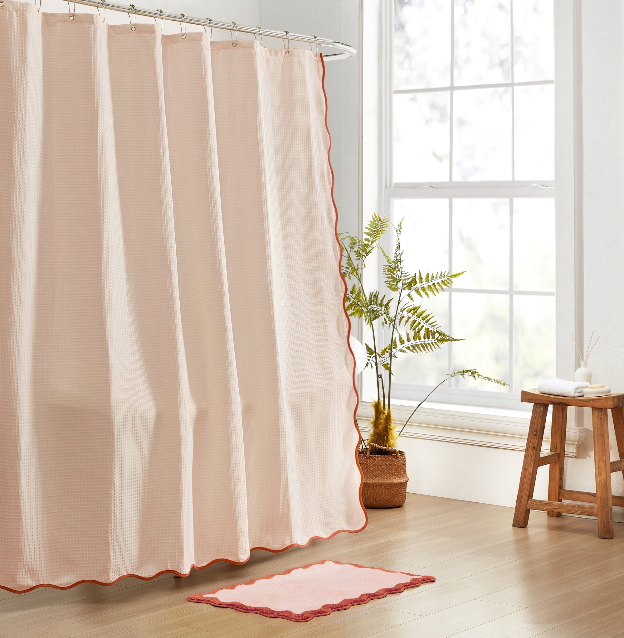 Beige shower curtain with red trim in a bathroom setting with a plant and stool.