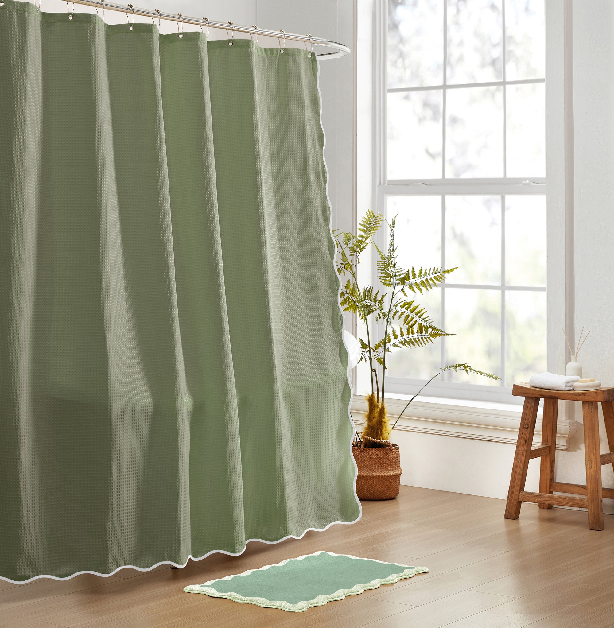 Green shower curtain in a bathroom with a plant and stool.