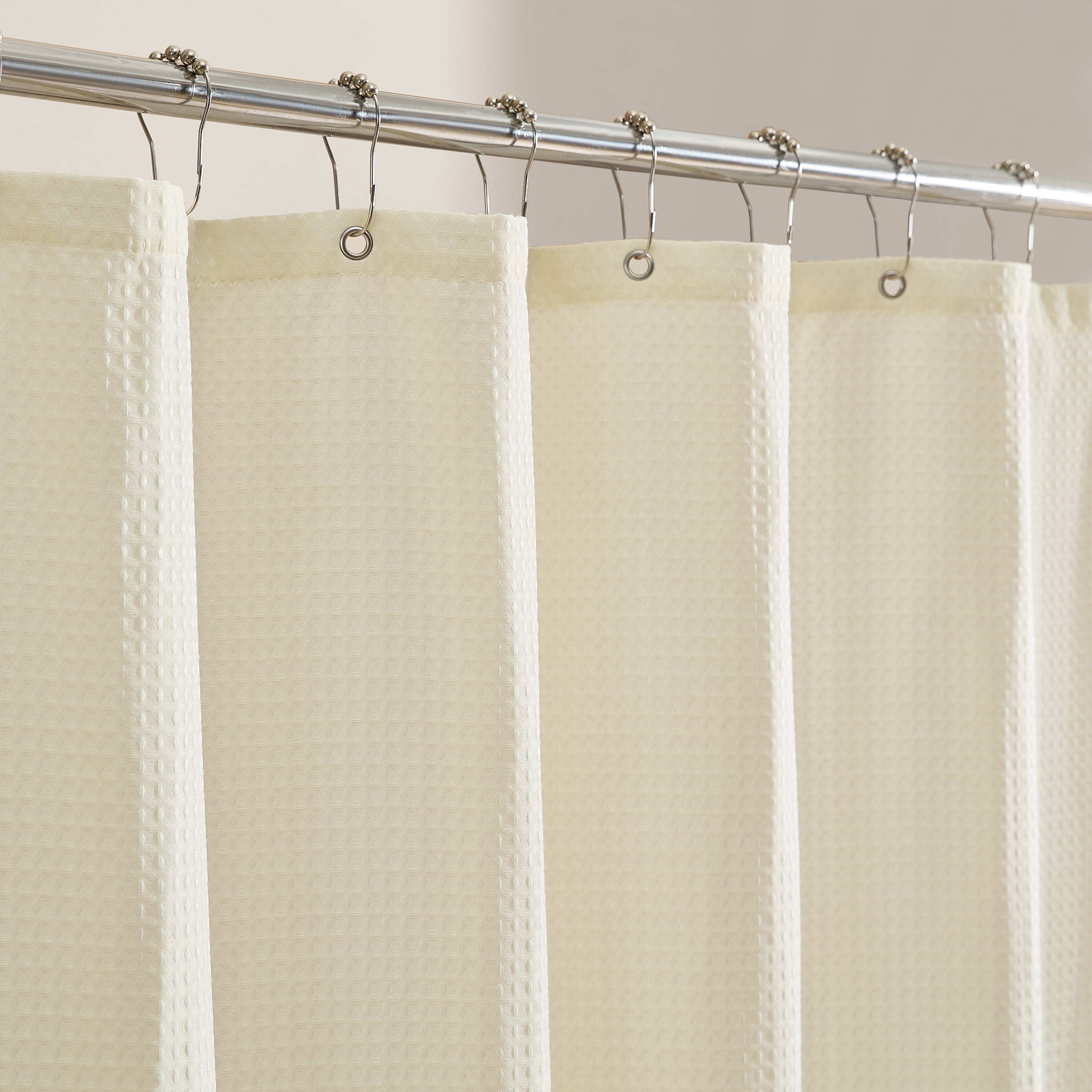 Beige shower curtain with a textured pattern on a metal rod.