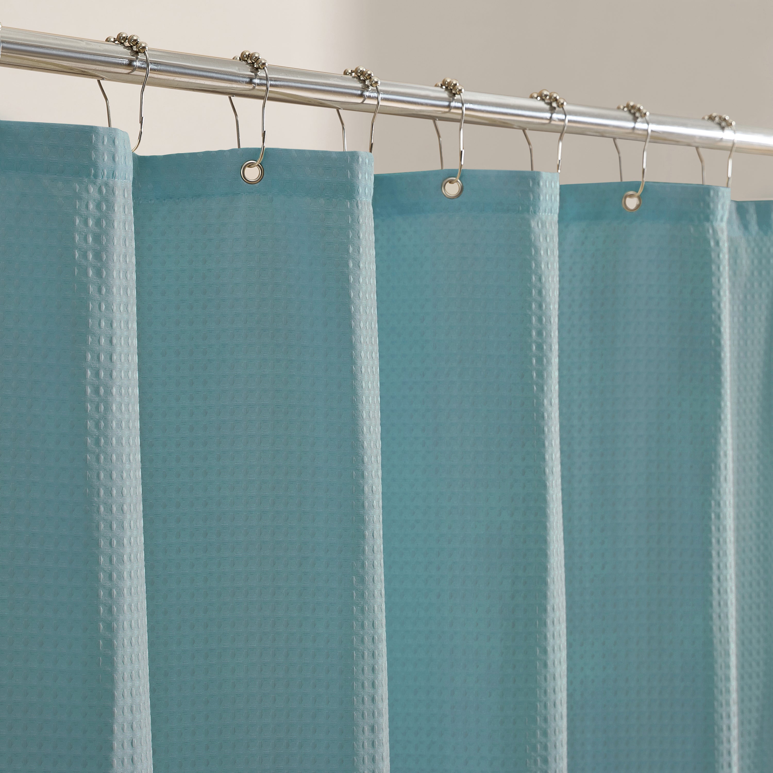 Teal shower curtain with a textured pattern on a silver curtain rod.