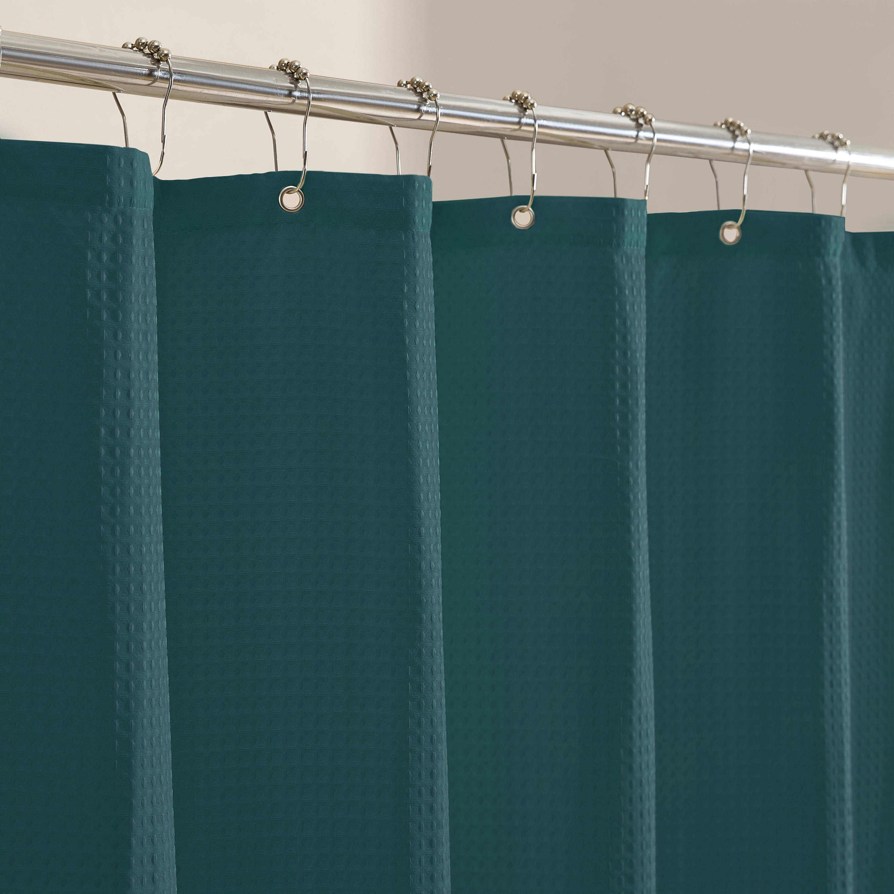 Teal shower curtain with silver hooks on a gray wall background