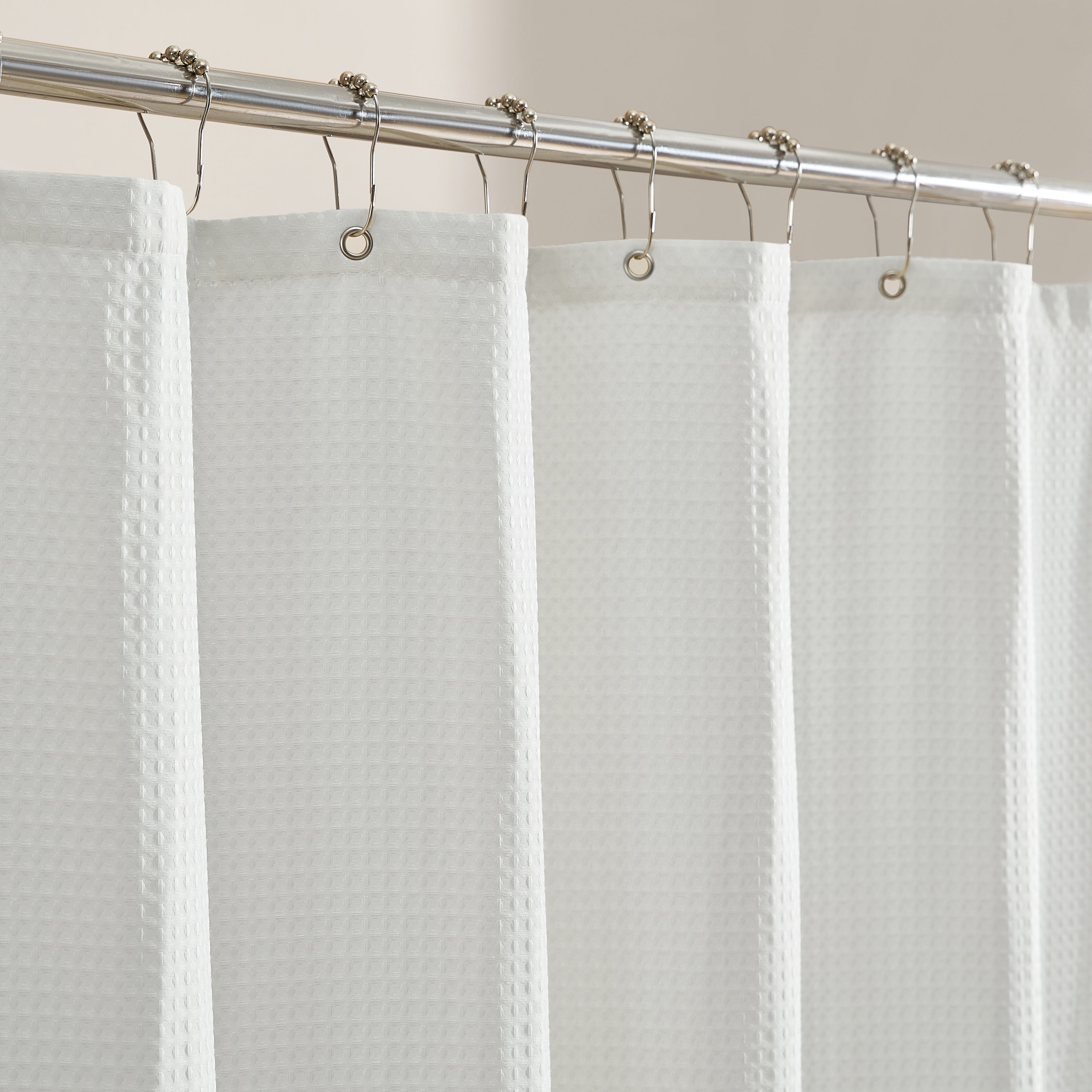 White textured shower curtain with silver hooks on a beige wall.