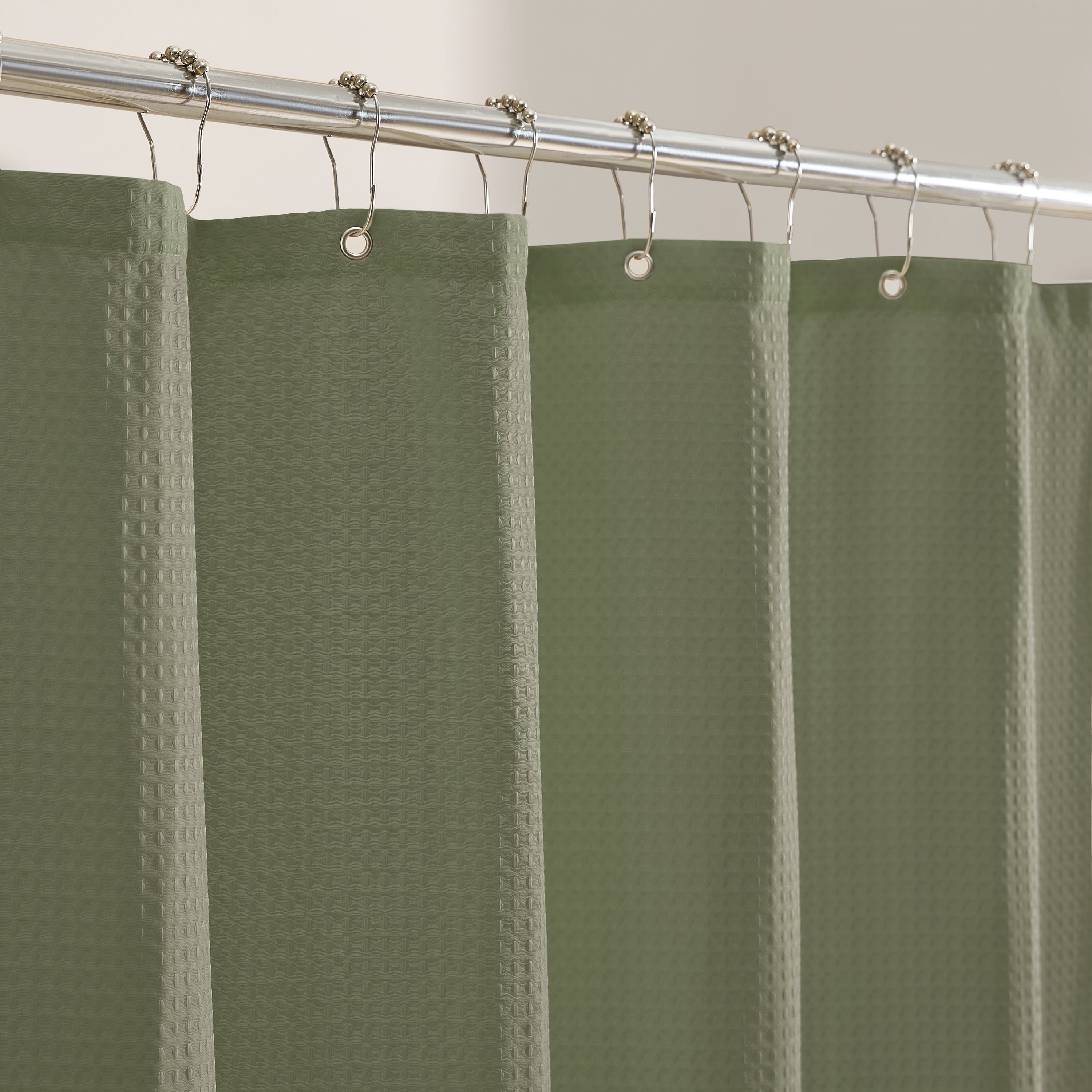 Green shower curtain with waffle texture hanging on a silver curtain rod.