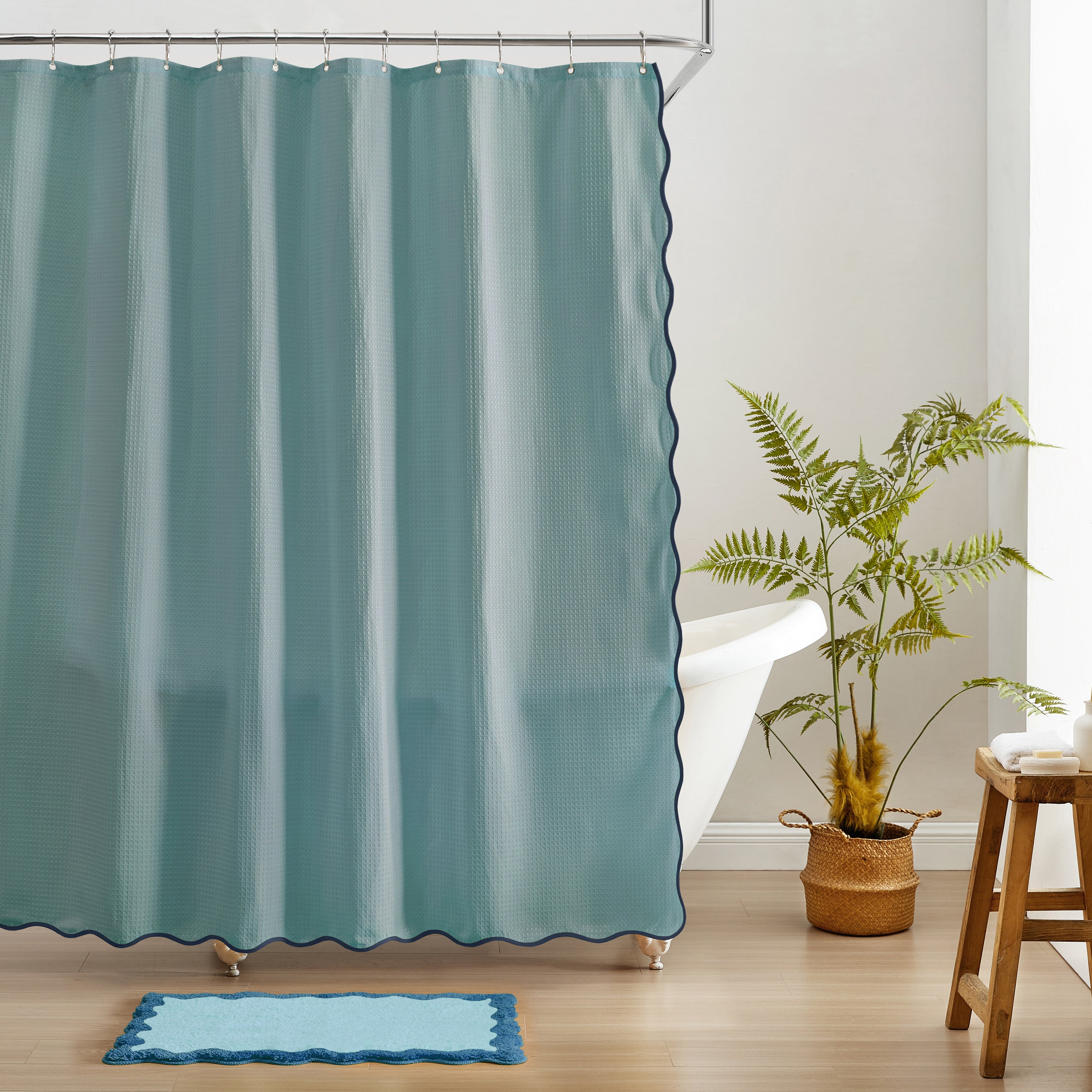 Teal shower curtain with scalloped edge in a bathroom setting with a plant and stool.