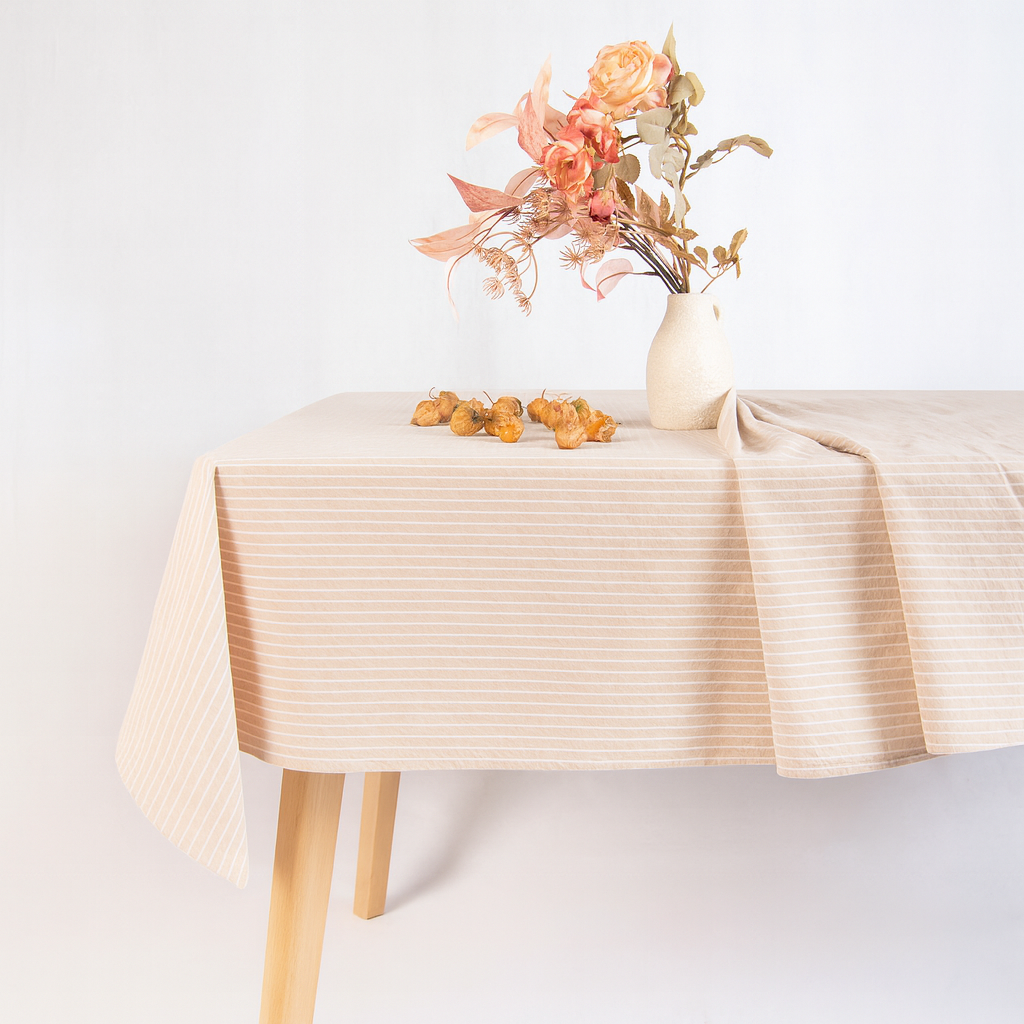 Beige tablecloth on a wooden table with a vase of flowers and small oranges.
