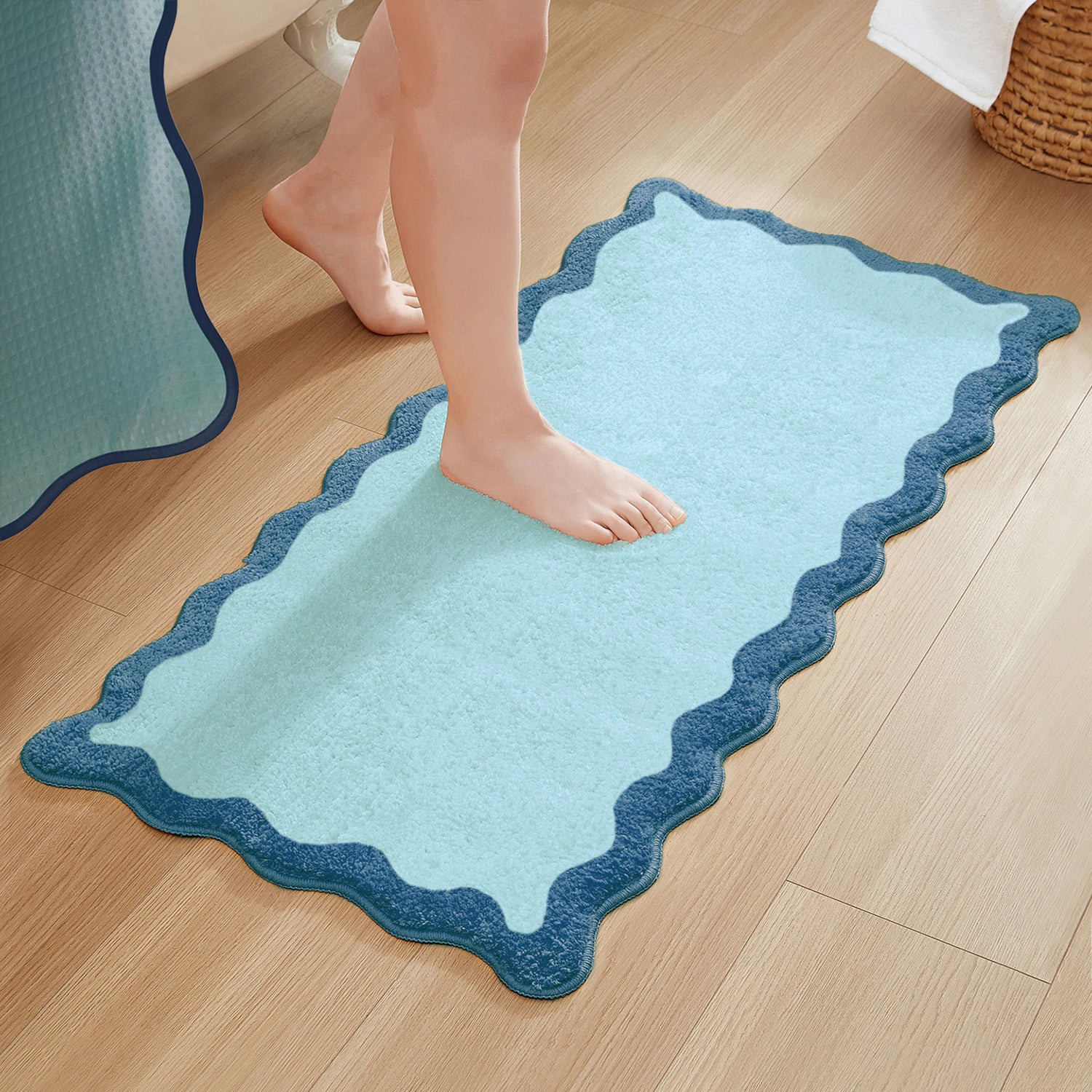 Light blue bath mat with scalloped edge on a wooden floor, person stepping onto it.