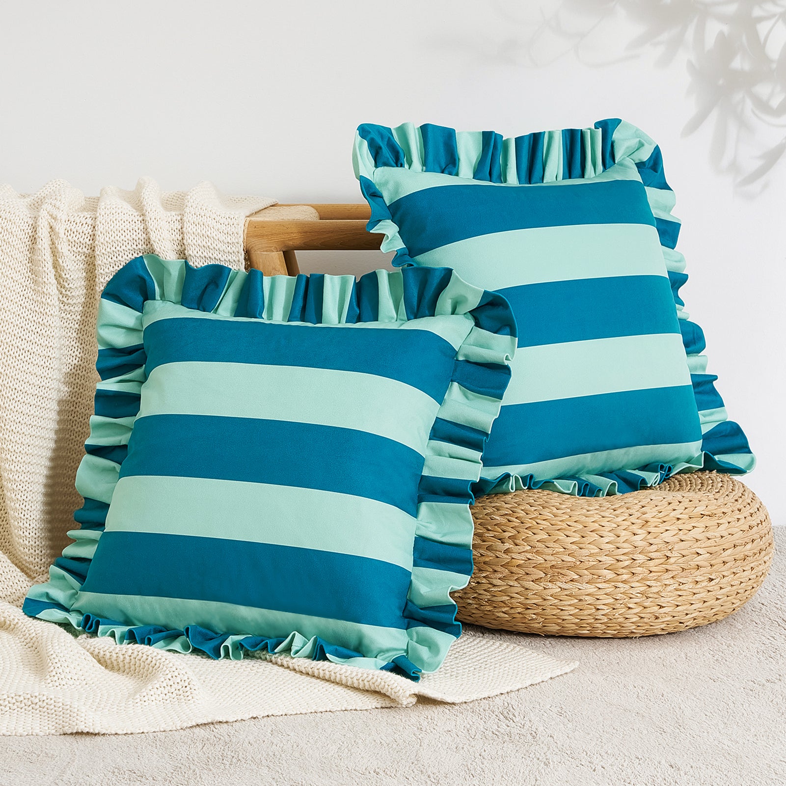 Two blue and green striped pillows with ruffled edges on a neutral background