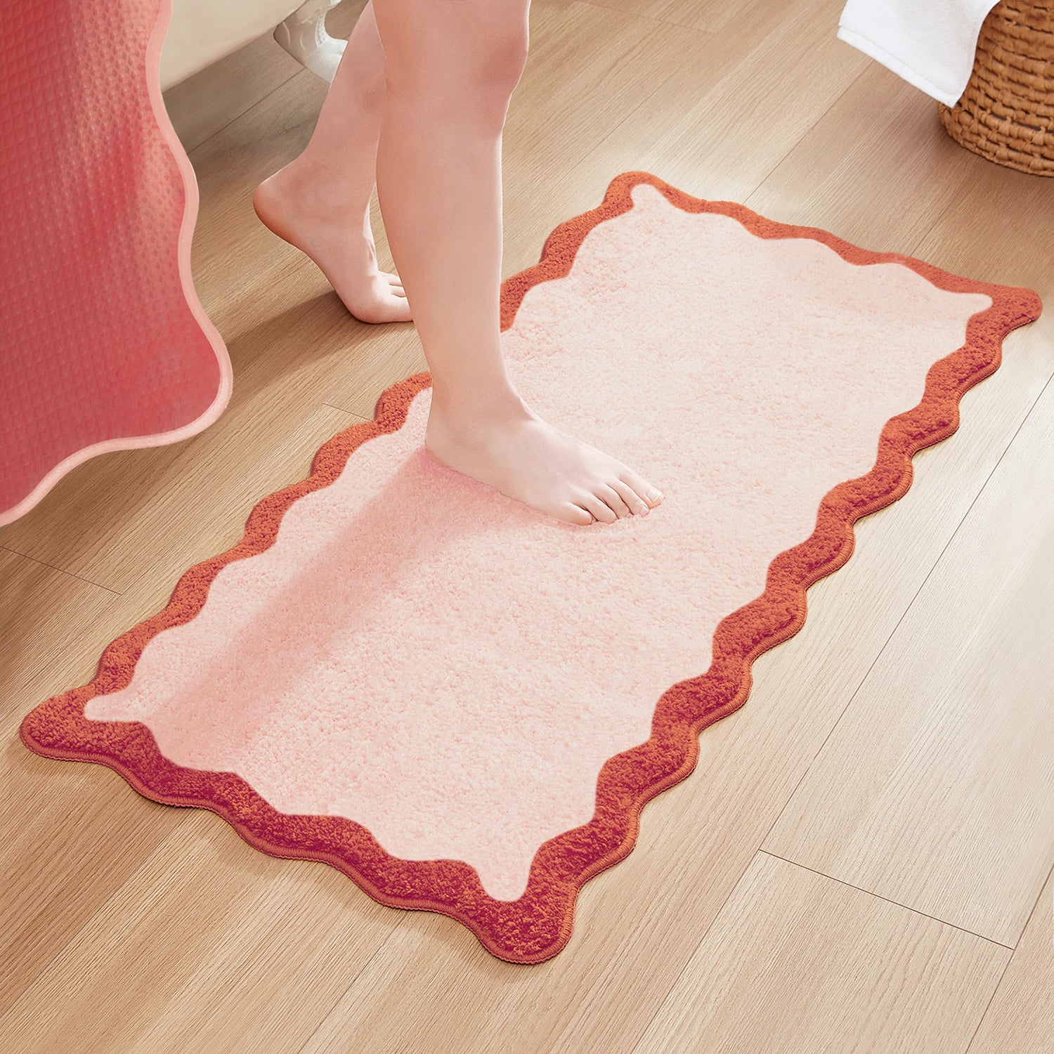 Pink bath mat with red border on a wooden floor