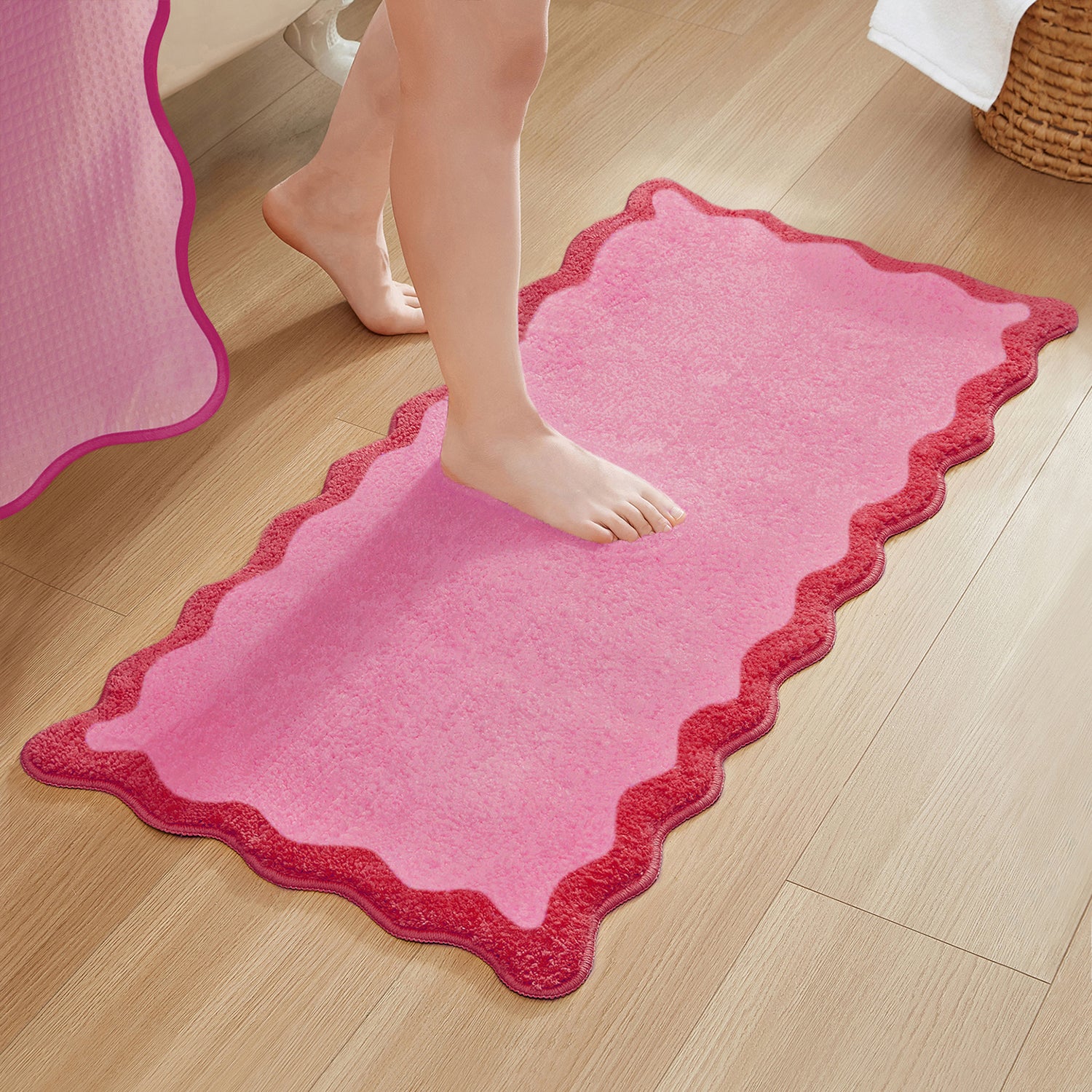 Pink bath mat with scalloped edge on a wooden floor