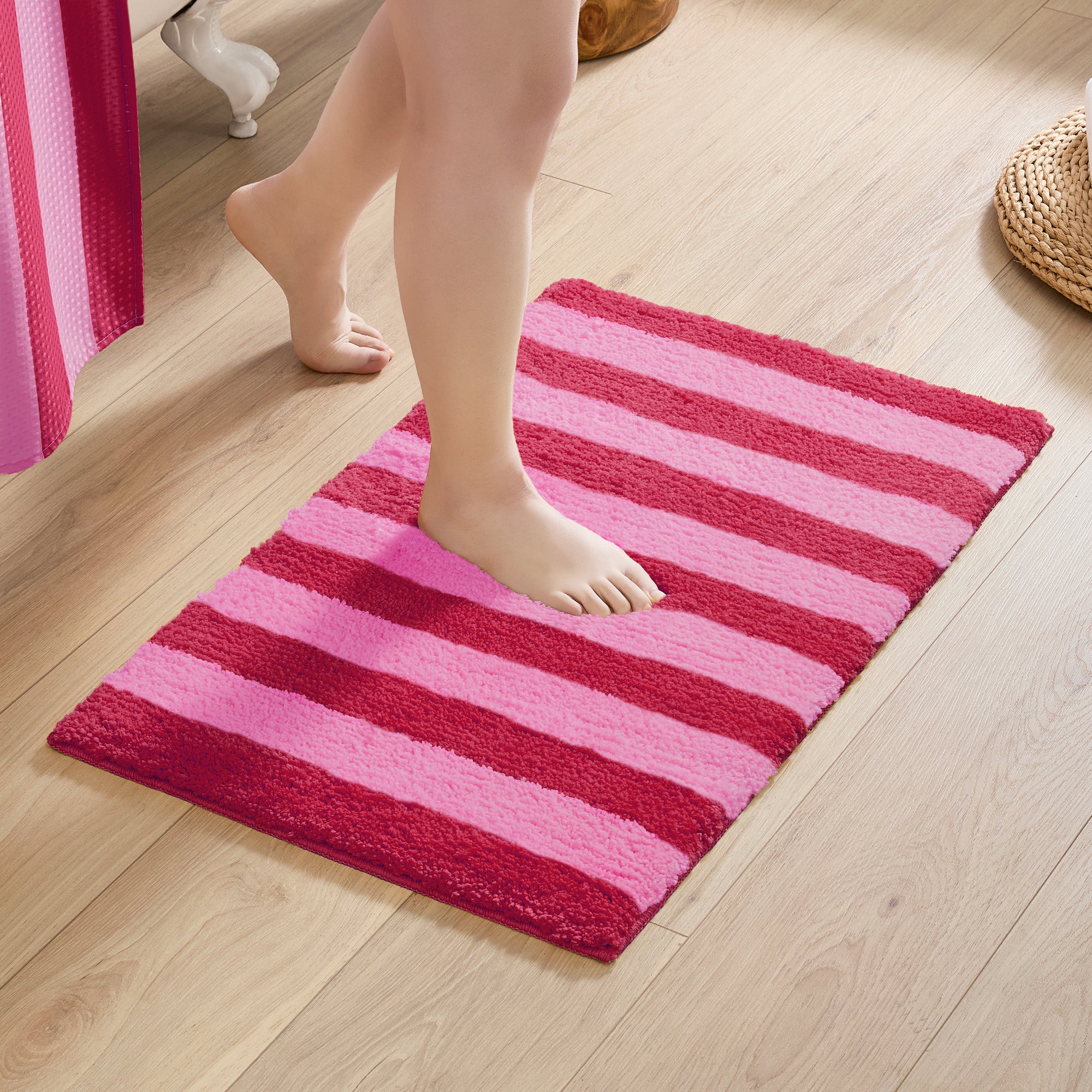 Person stepping onto a pink and red striped bath mat on a wooden floor.
