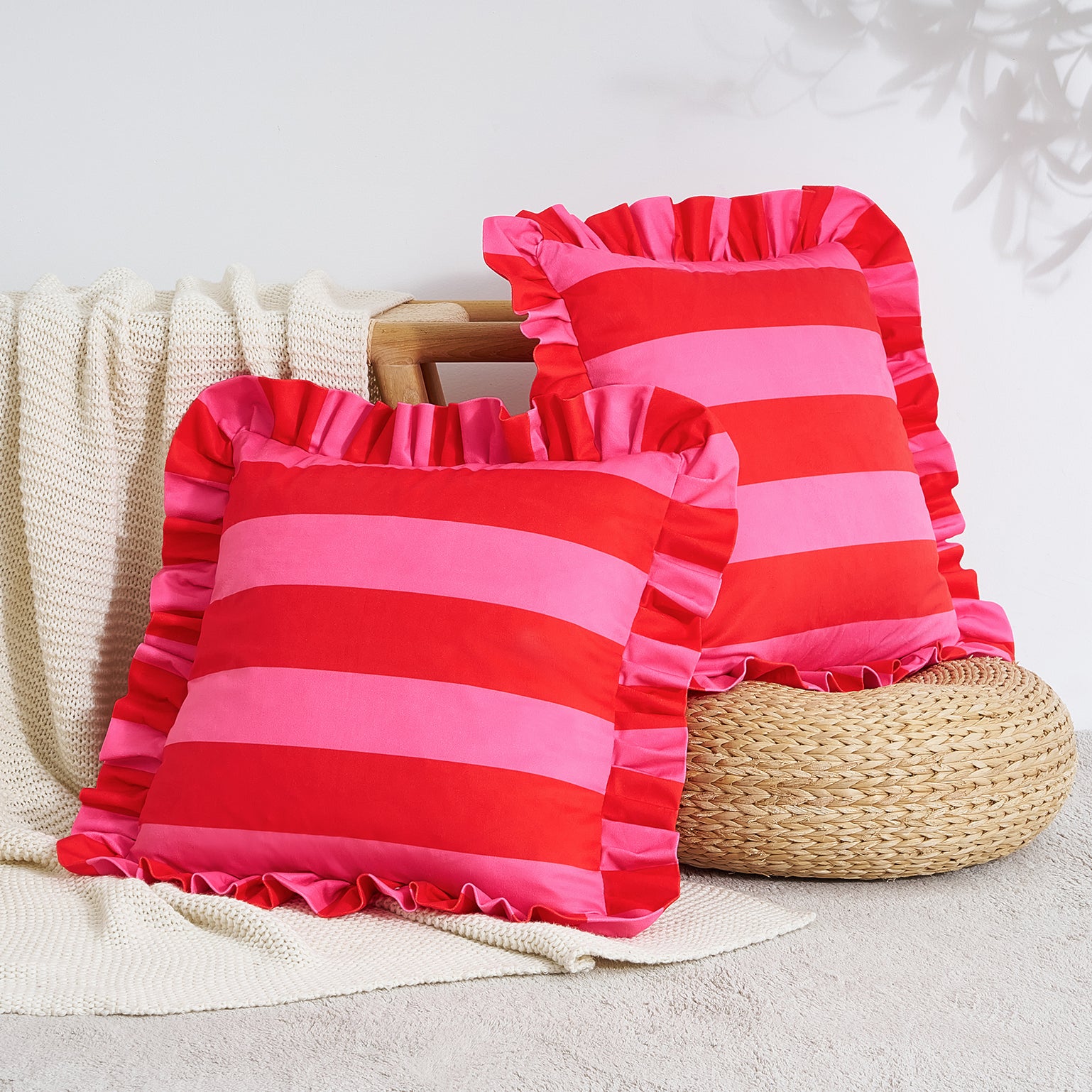 Two pink and red striped pillows with ruffled edges on a textured surface.