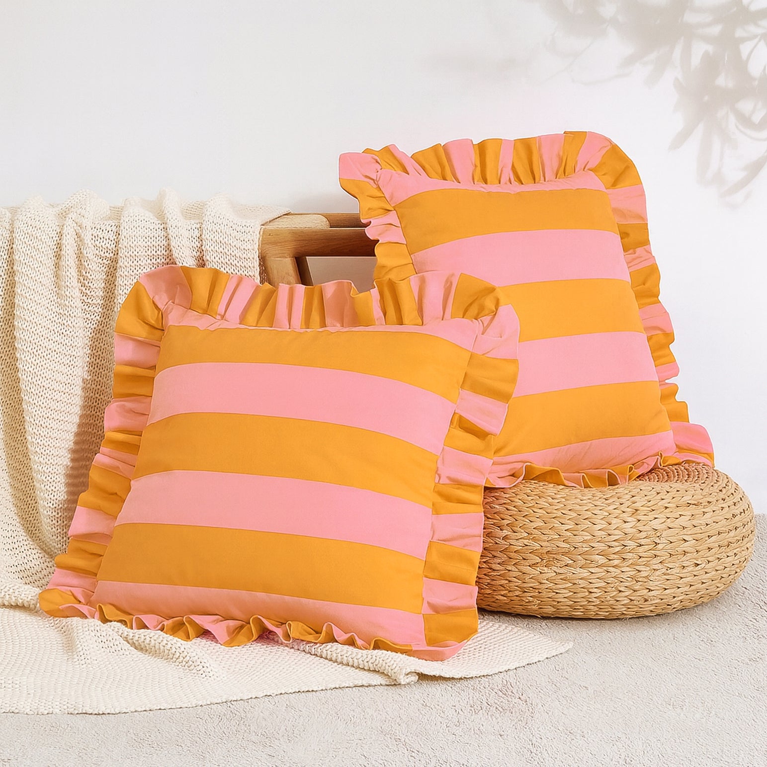 Pink and orange striped pillows with ruffles on a neutral background