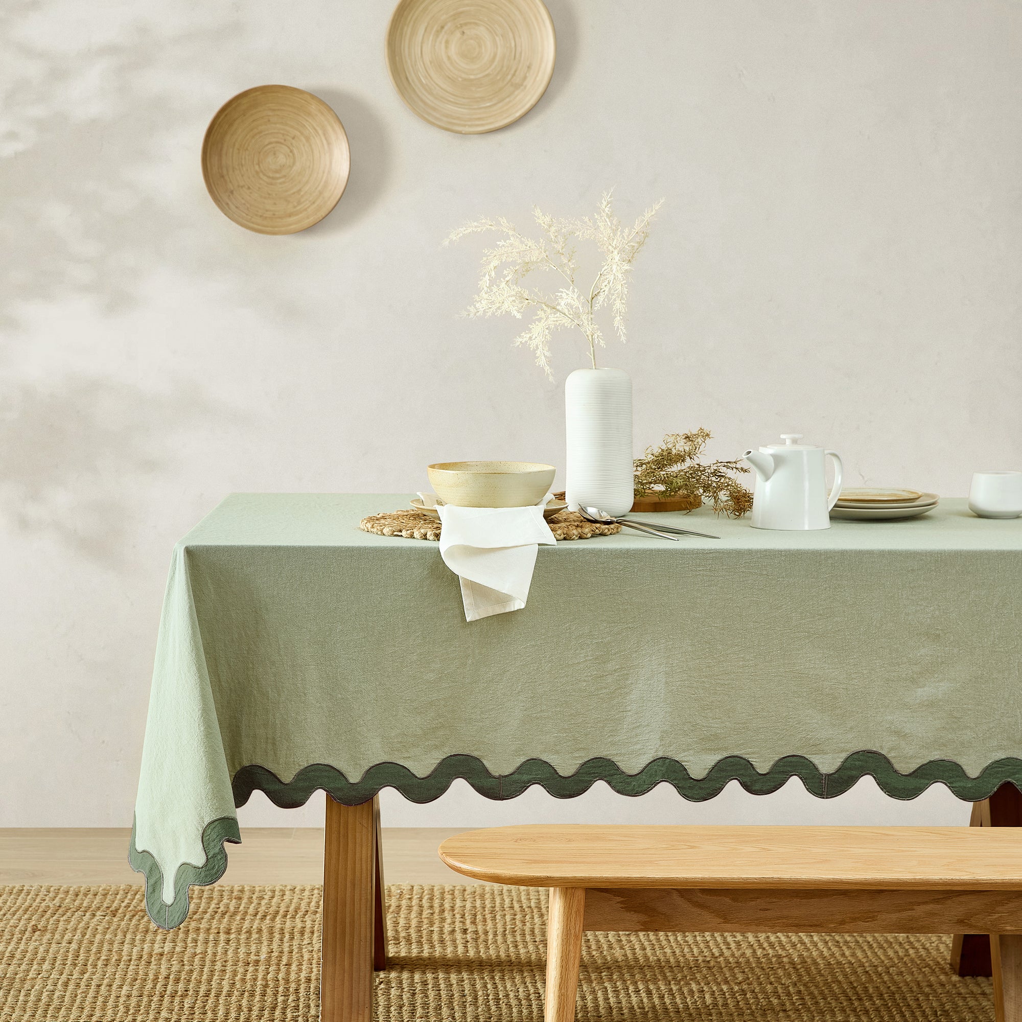 Table with a green tablecloth, white candle, and decorative items against a neutral wall.