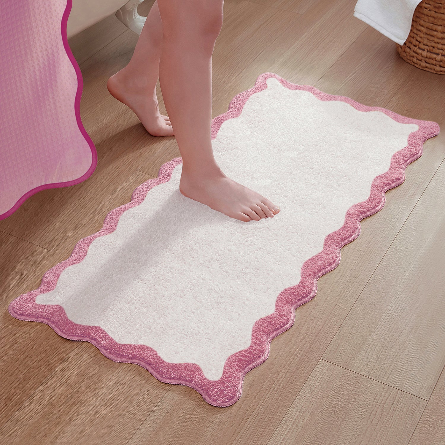 White bath mat with pink border on a wooden floor, person stepping onto it.