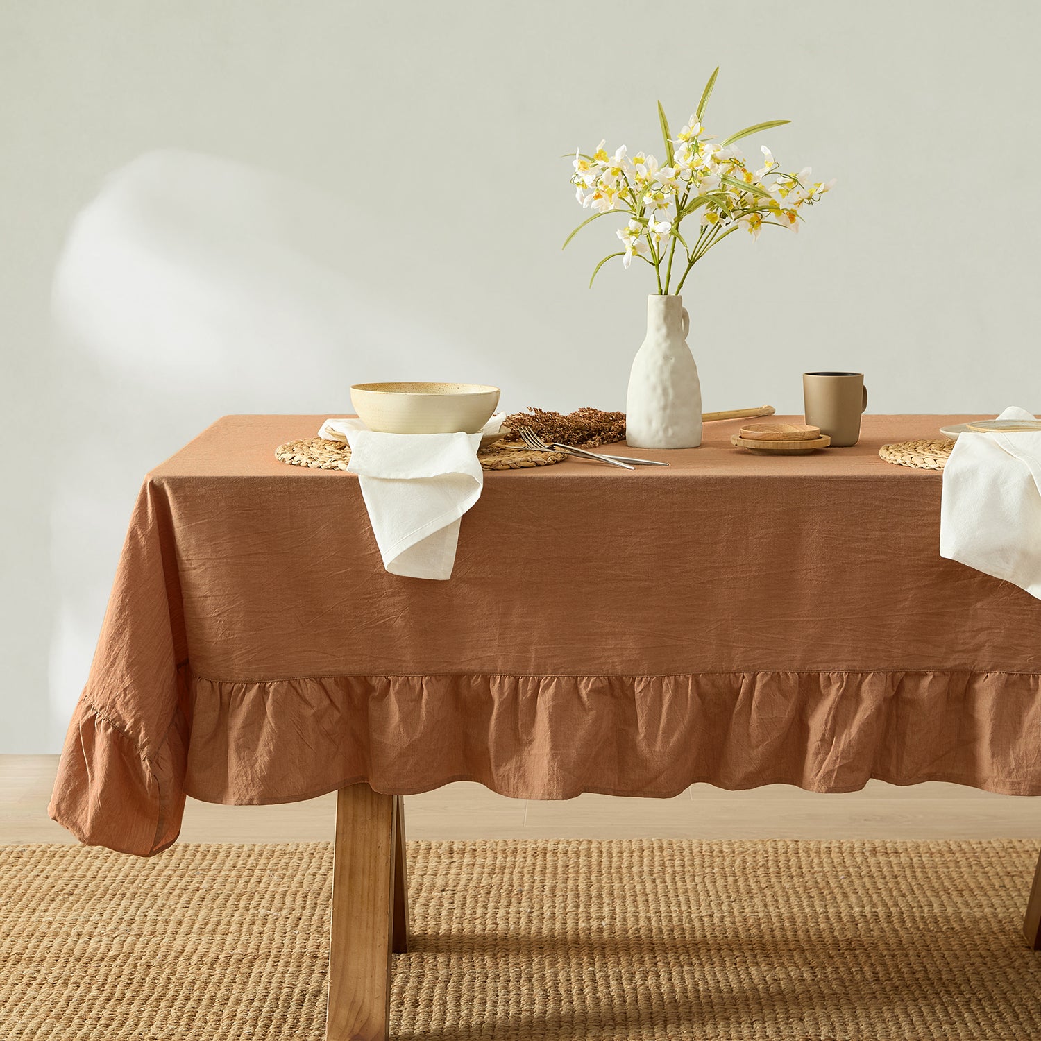 Table with a brown tablecloth, white vase with flowers, and decorative items on a neutral background