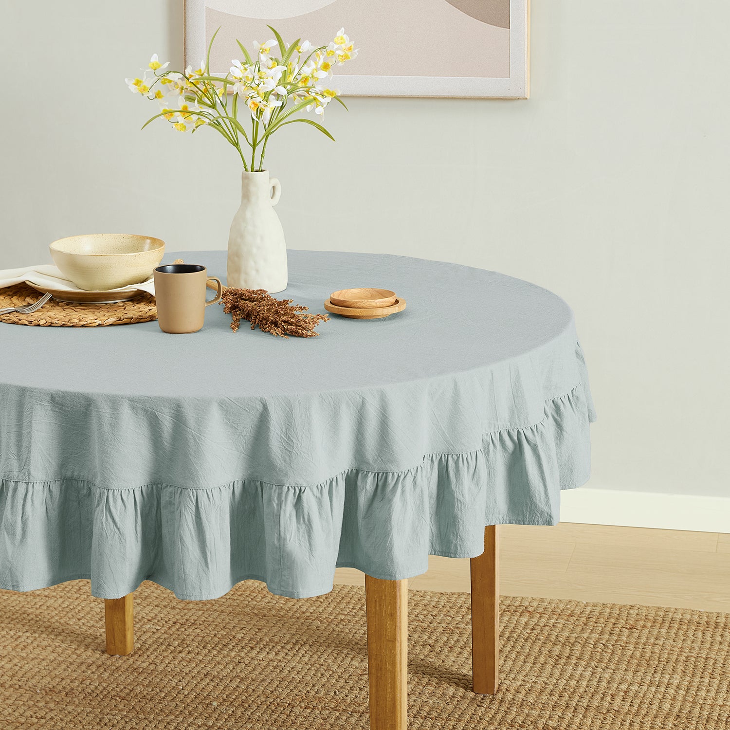 Round table with a light blue tablecloth, vase with flowers, and decorative items in a room.