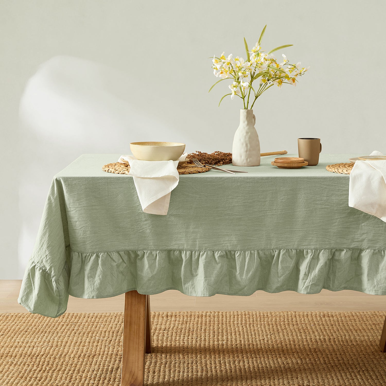 Table with a green tablecloth, white vase with flowers, and various items on a neutral background