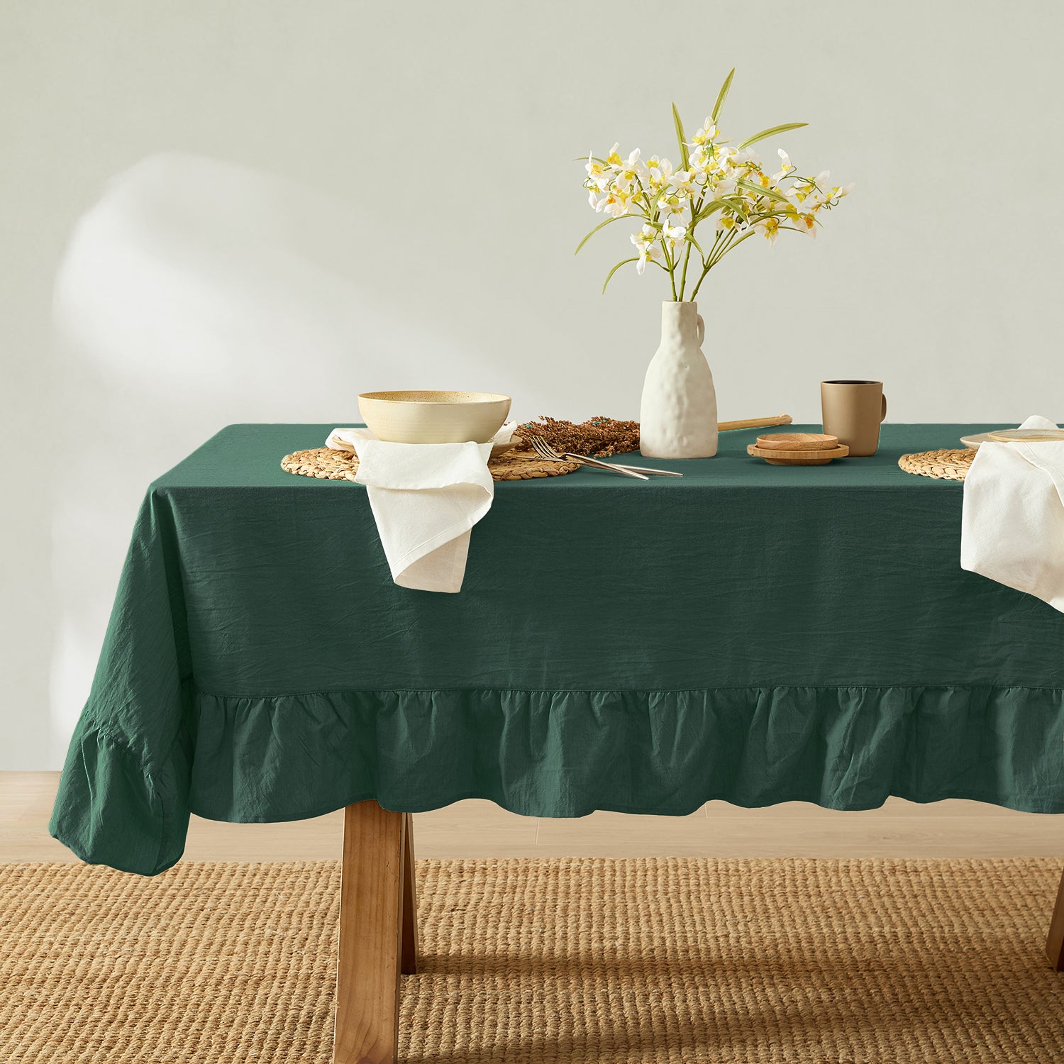Green tablecloth on a table with a vase of flowers and other items against a plain background