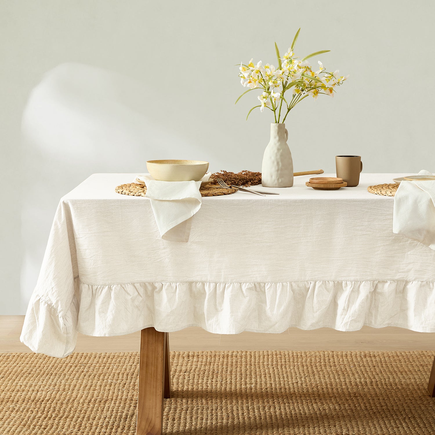 Dining table with a white tablecloth, vase with flowers, and decorative items on a neutral background