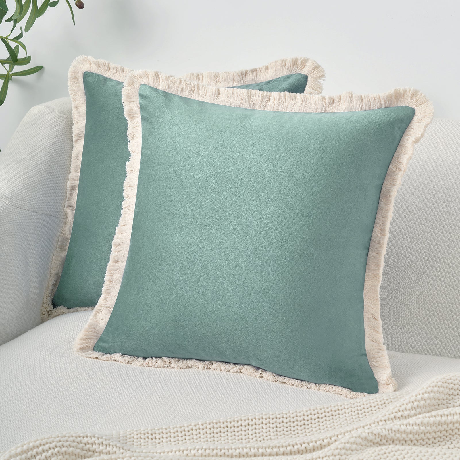 Teal pillows with beige fringes on a light gray sofa.