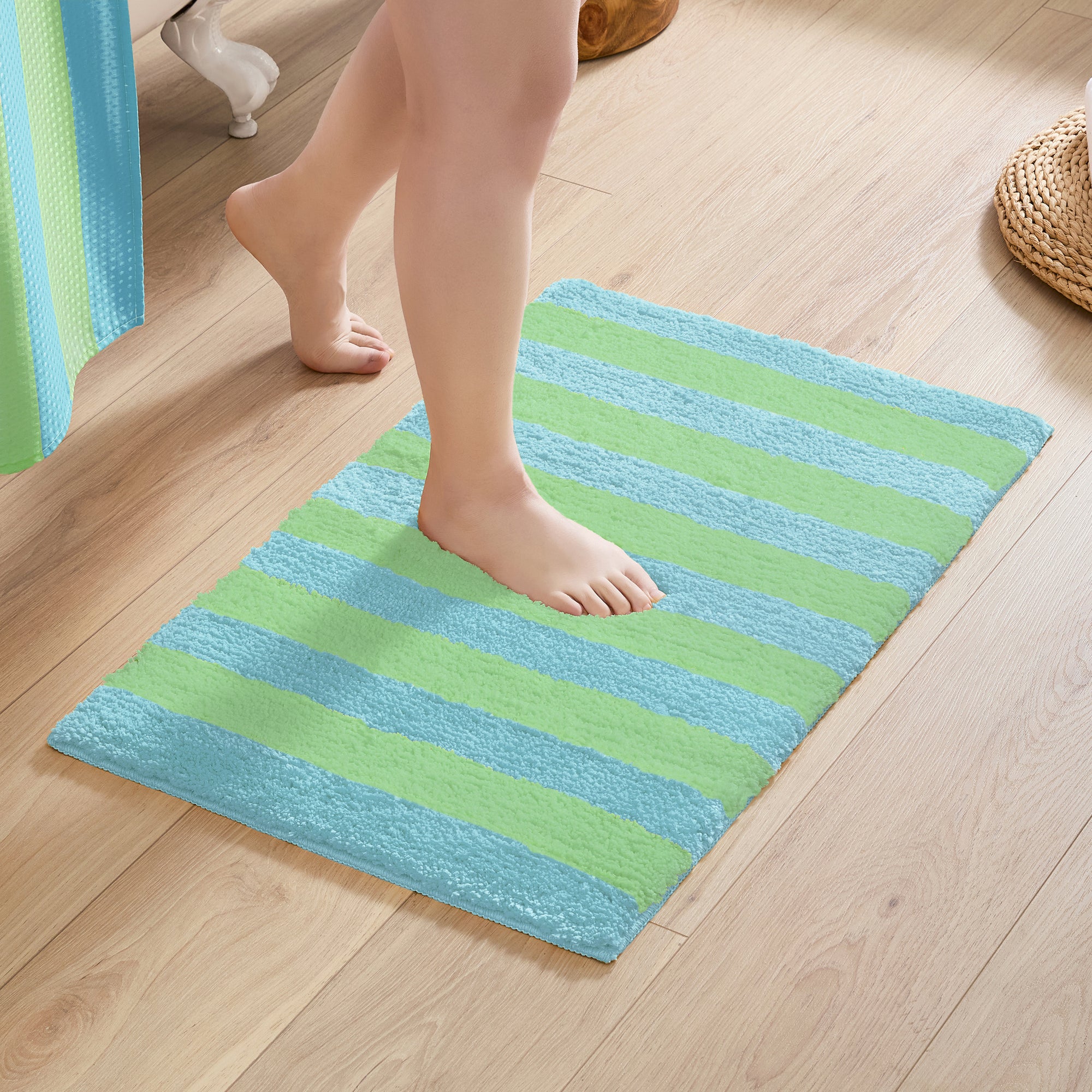Person stepping onto a green and blue striped bath mat on a wooden floor.
