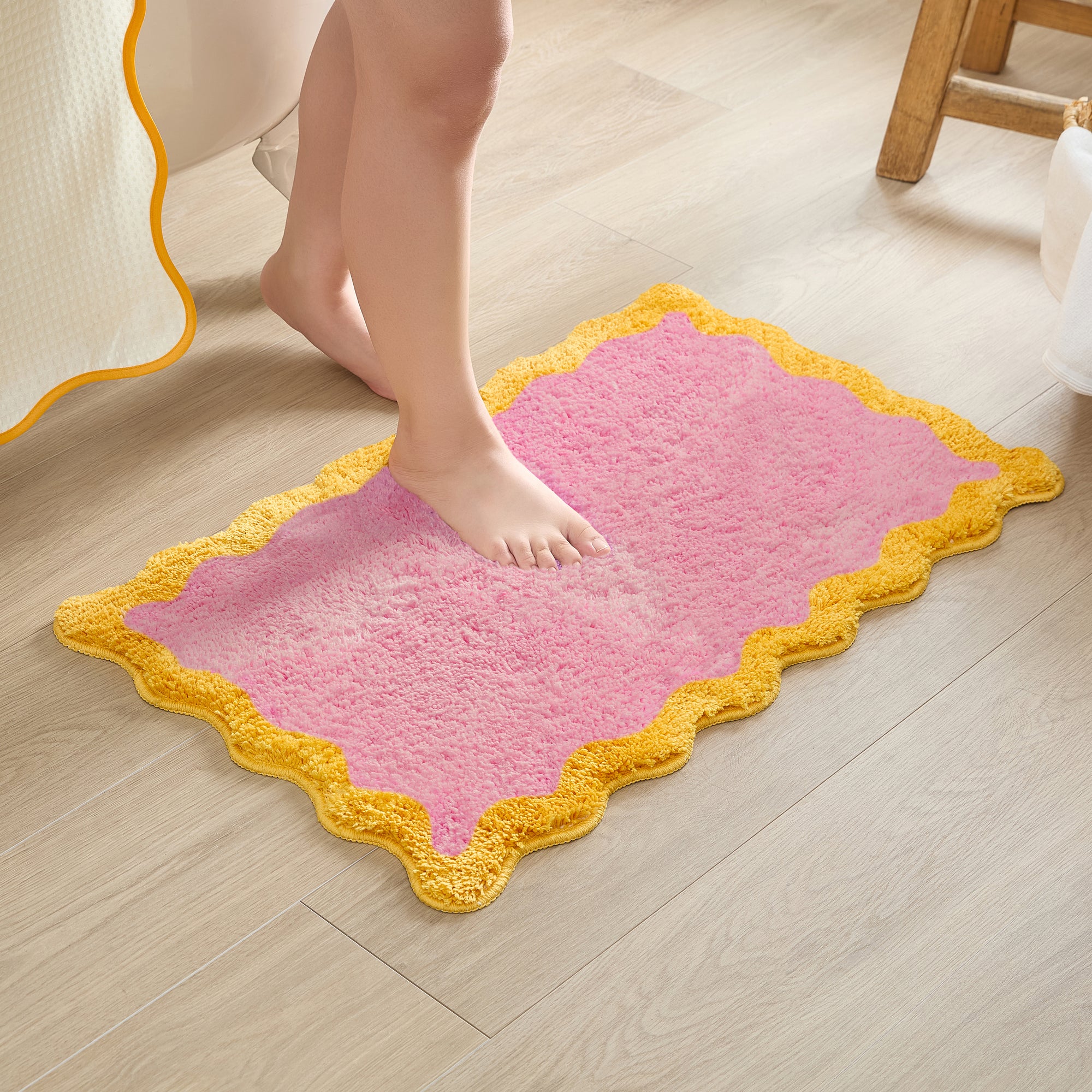Pink bath mat with yellow border on a wooden floor, person stepping onto it.