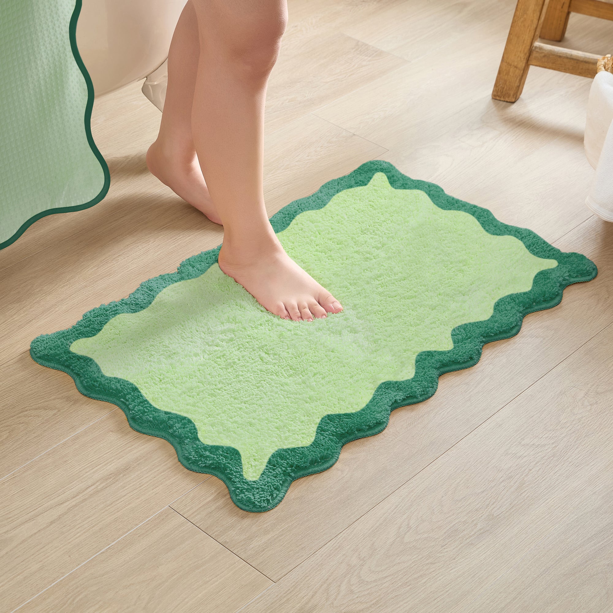 Green bath mat on a wooden floor with a person stepping onto it.