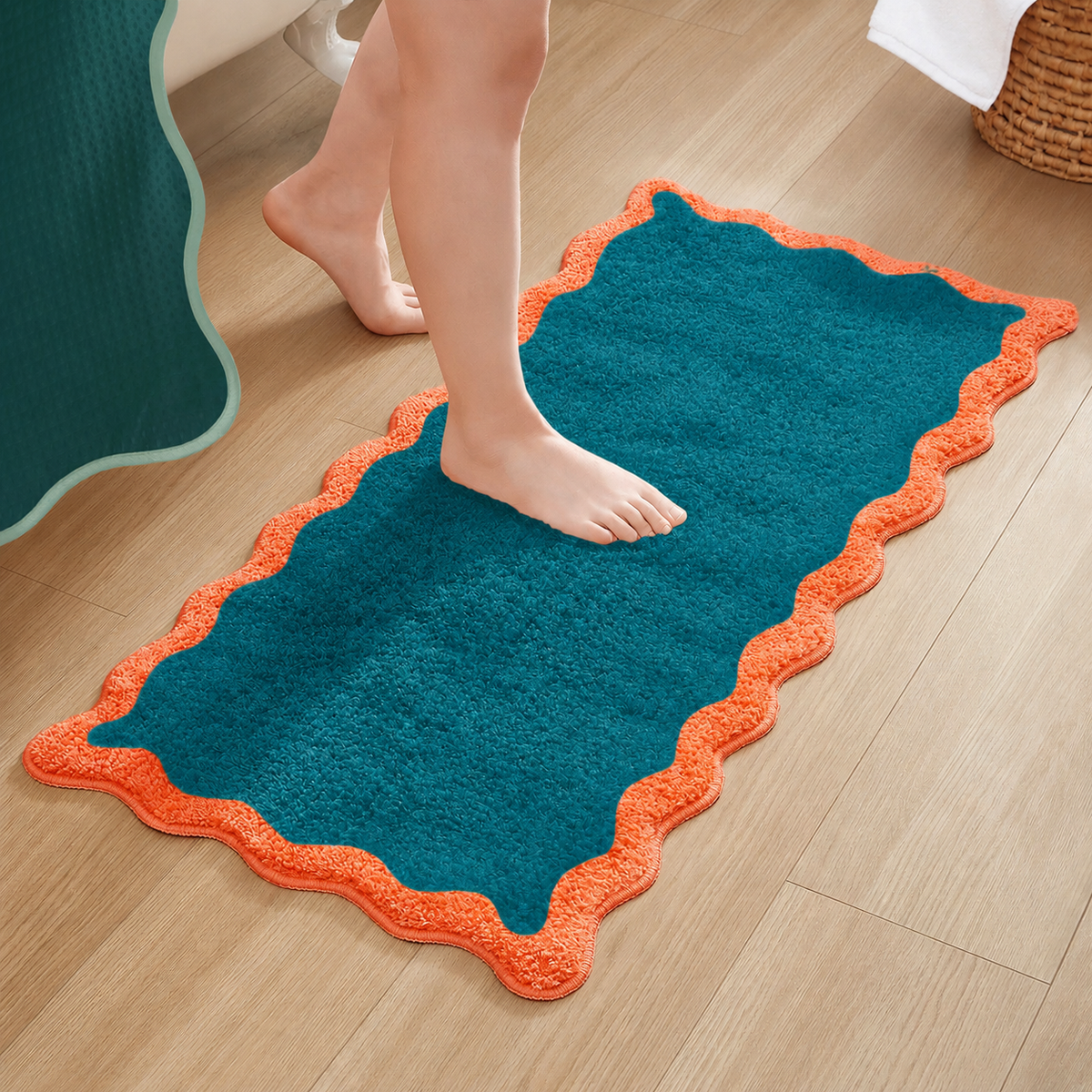 A rectangular bath mat in teal with a bright orange scalloped border, shown on a light wood floor with a person's bare feet stepping on it.
