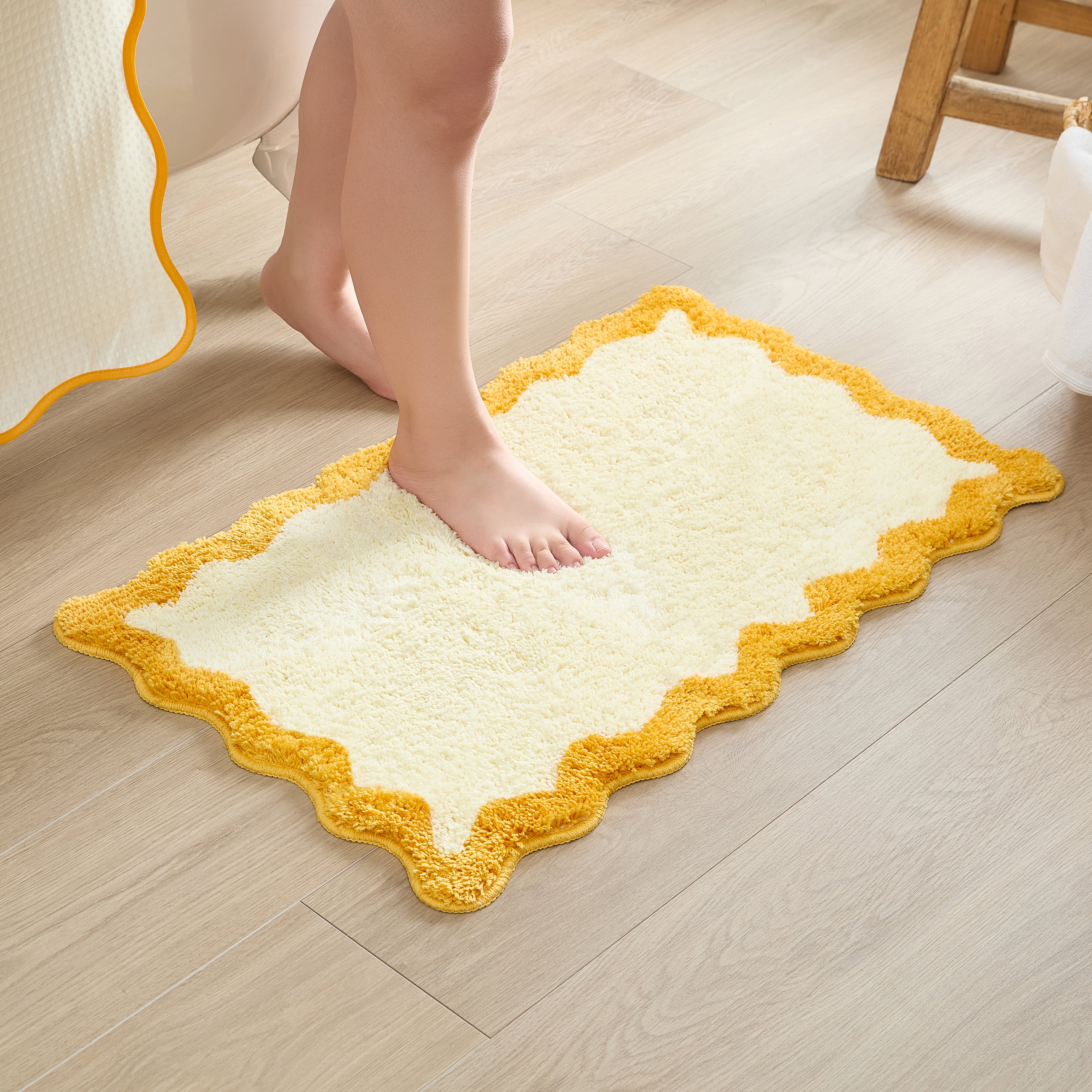 Yellow and white bath mat on a wooden floor with a person stepping onto it.