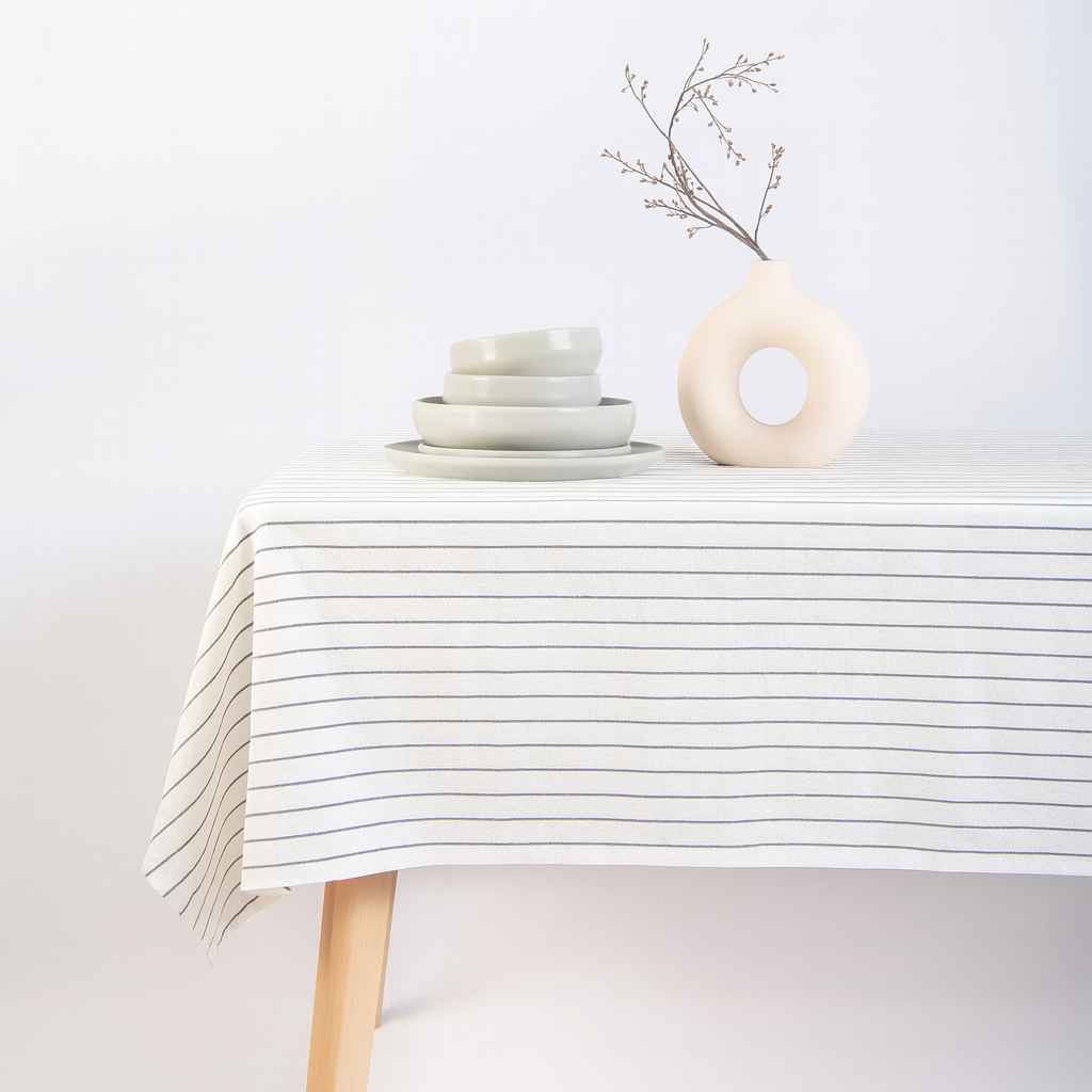 Table with striped tablecloth, ceramic bowls, and vase on a plain background