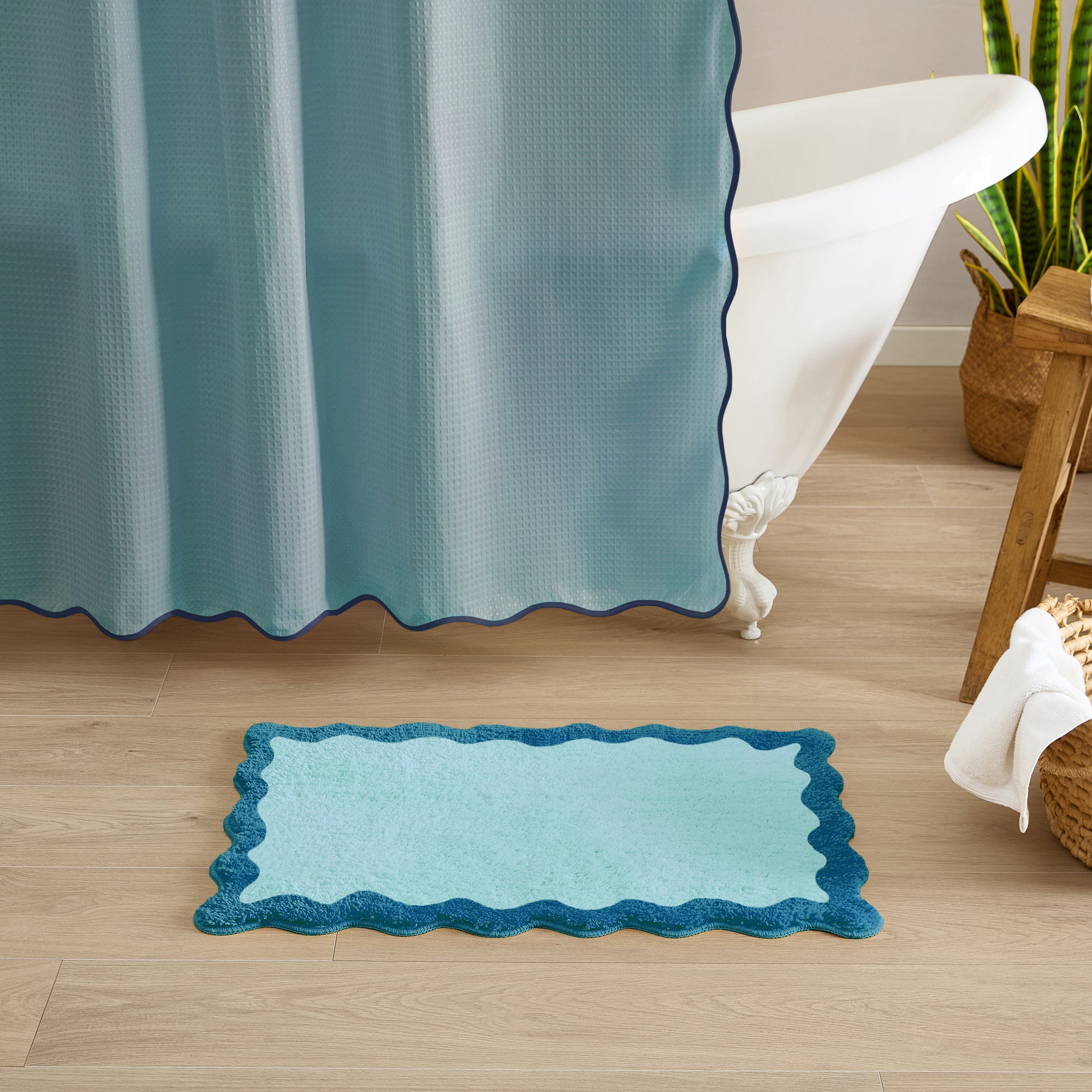 Blue bath mat on a wooden floor with a bathtub and shower curtain in the background.