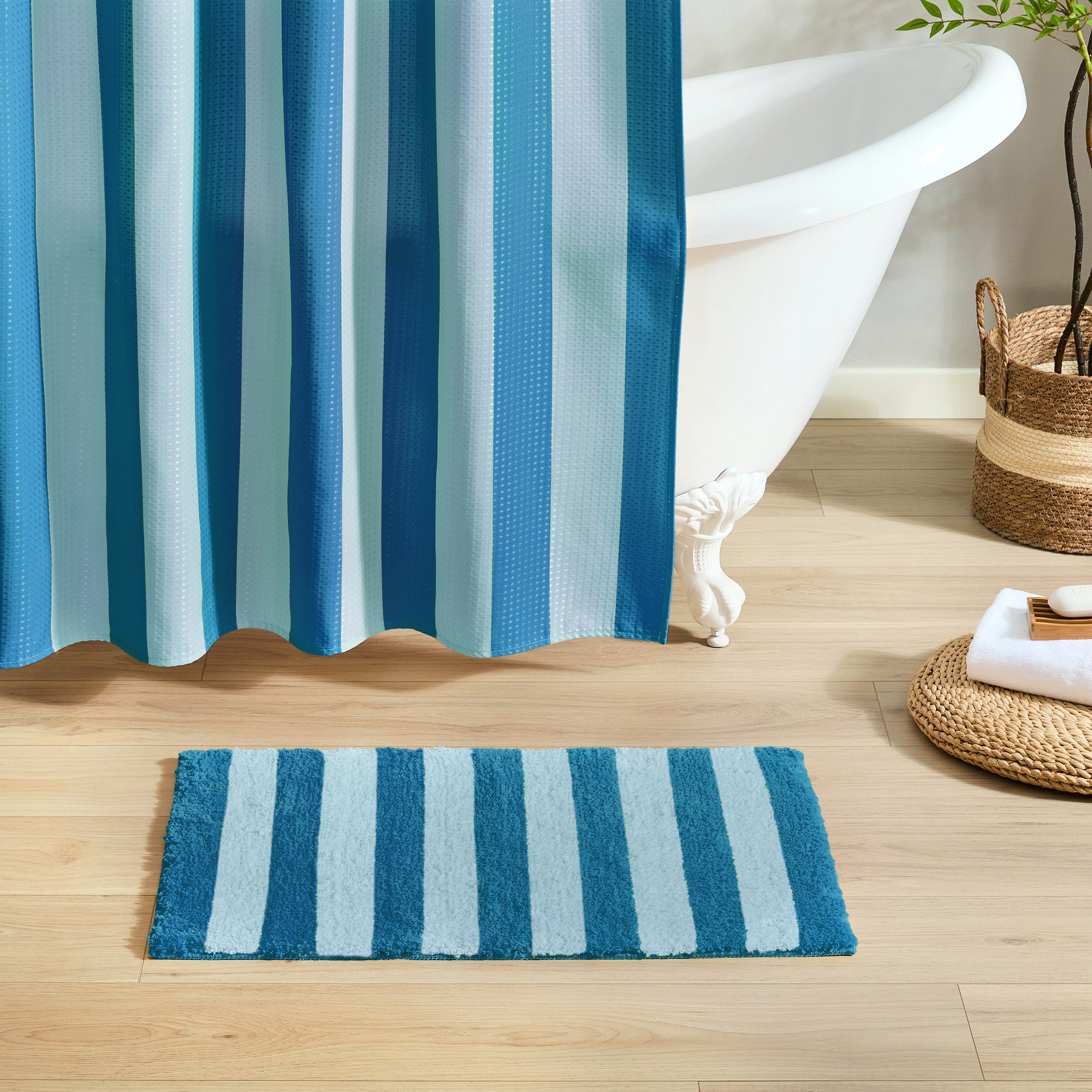 Blue and white striped shower curtain and bath mat on a wooden floor.