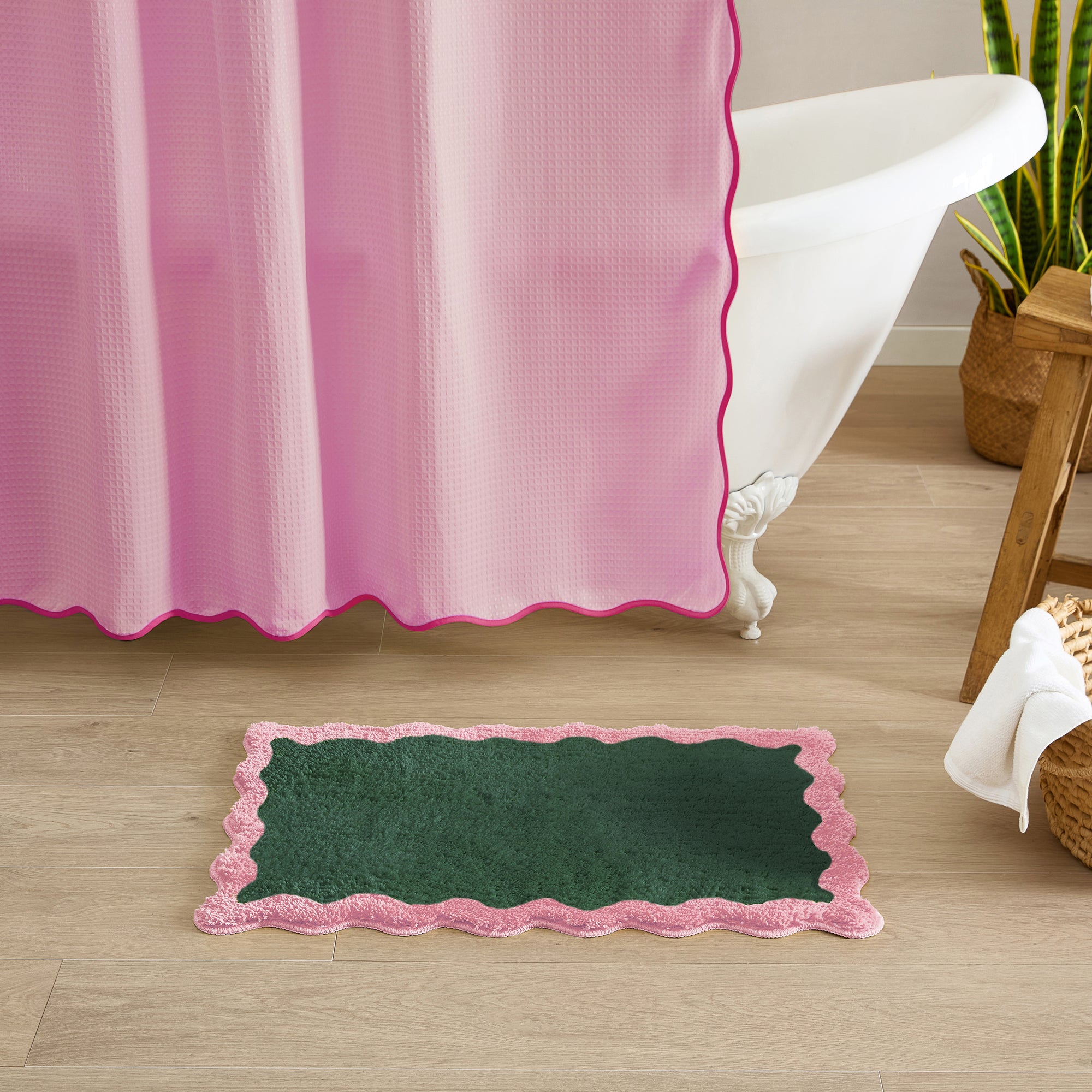 Green bath mat with pink border on wooden floor next to bathtub with pink shower curtain