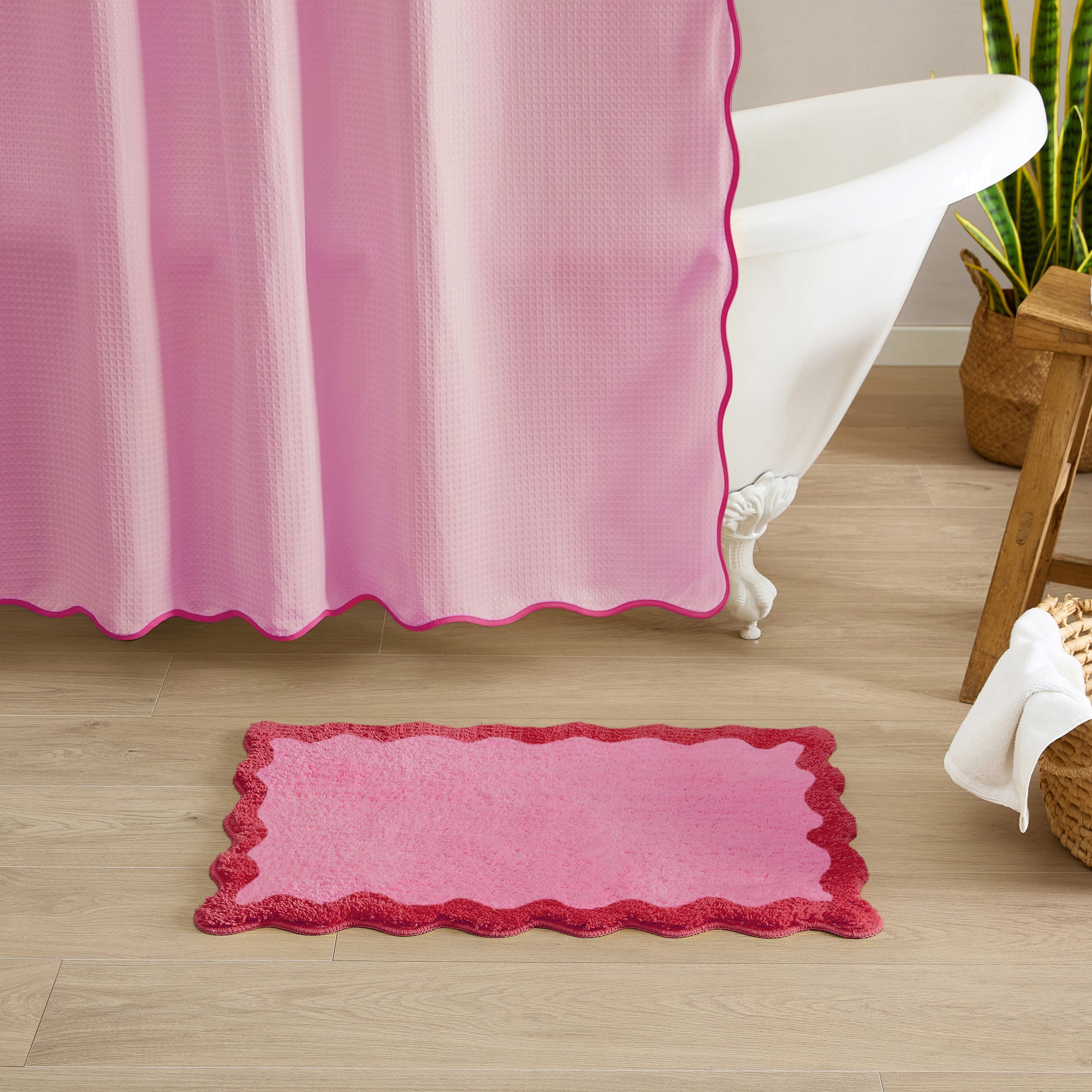 Pink bath mat on a wooden floor with a pink shower curtain in the background.